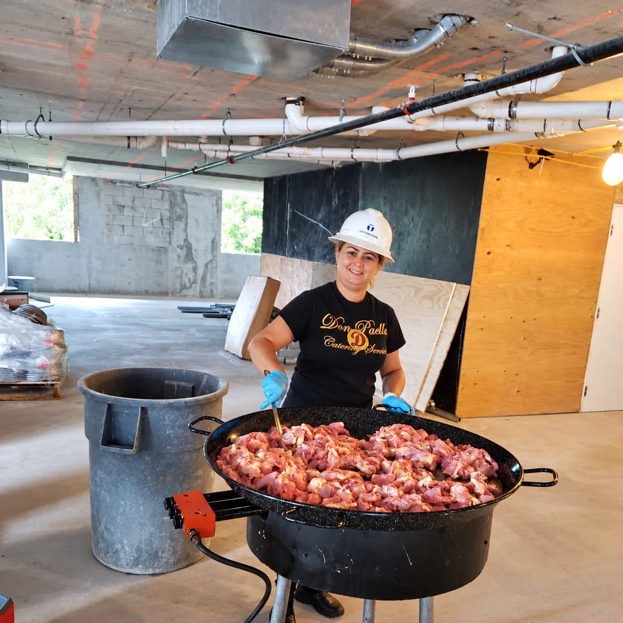 Chef Islaydis wearing a hard hat and blue gloves while cooking in a large pan at a Turner construction event.