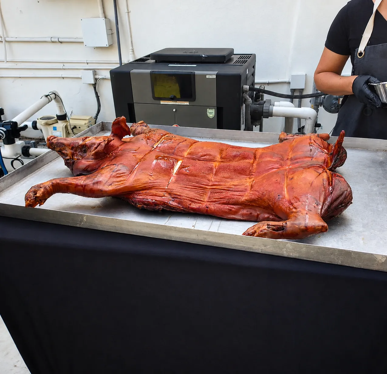 Whole lechón asado on a metal serving tray with a Don Paella team member behind it
