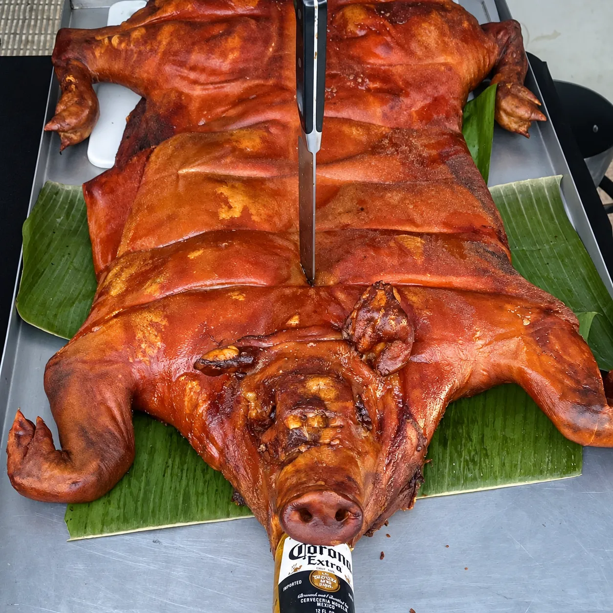 Whole lechón asado on banana leaves with a carving knife and bottle in the presentation
