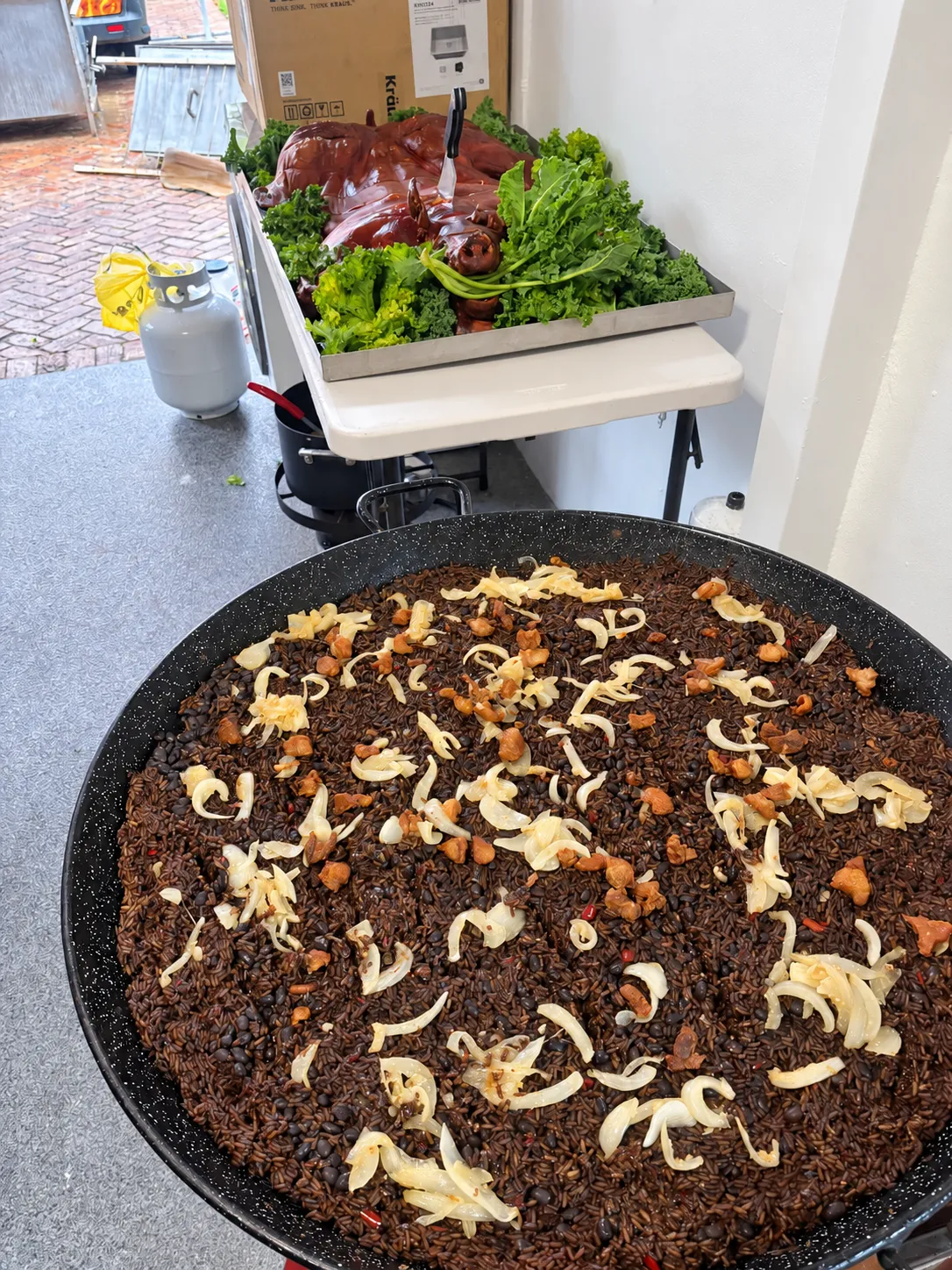 Arroz Moro topped with onions and pork pieces in a large pan beside a whole lechón asado