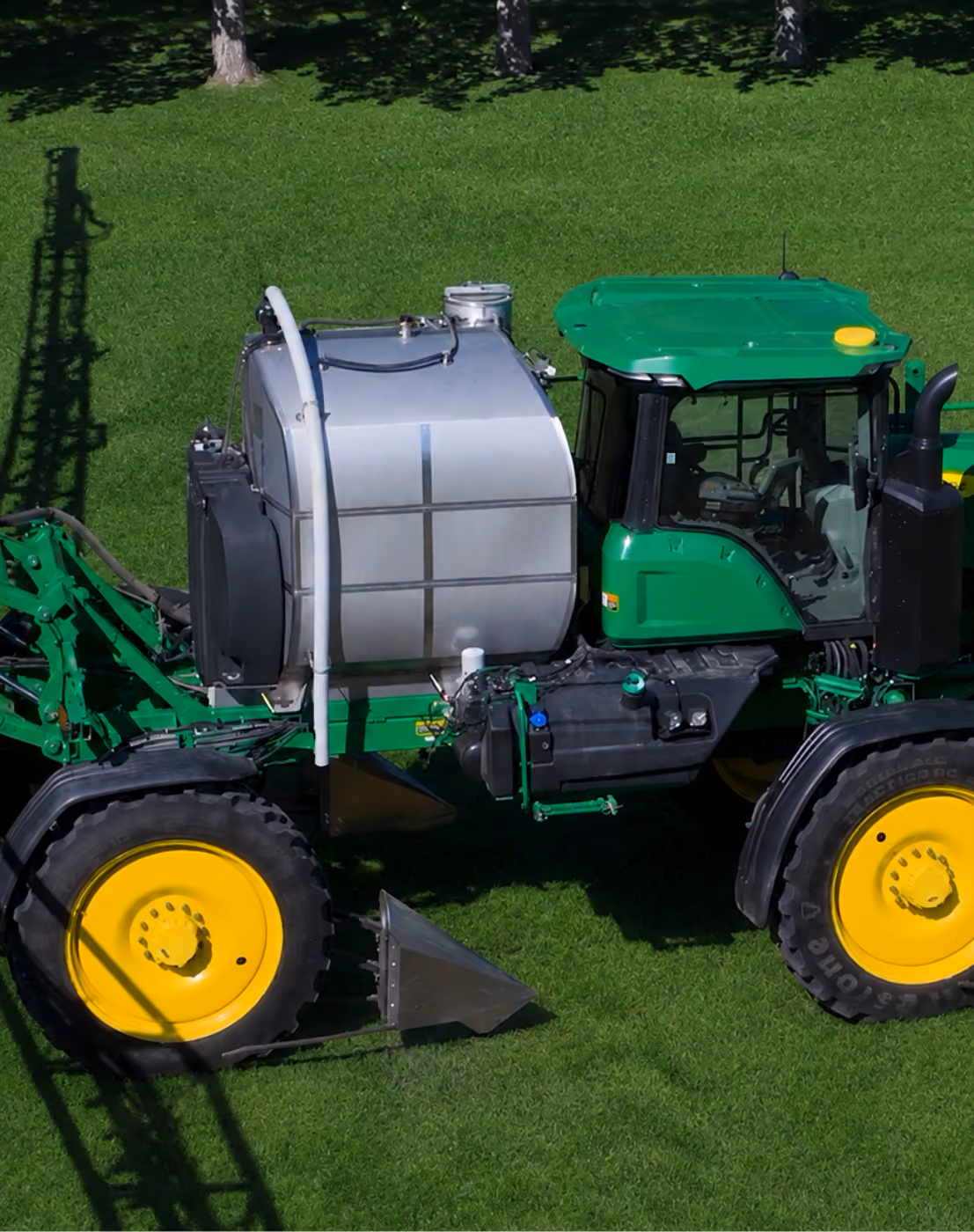Green tractor in a grass field with a sprayer modification attachment