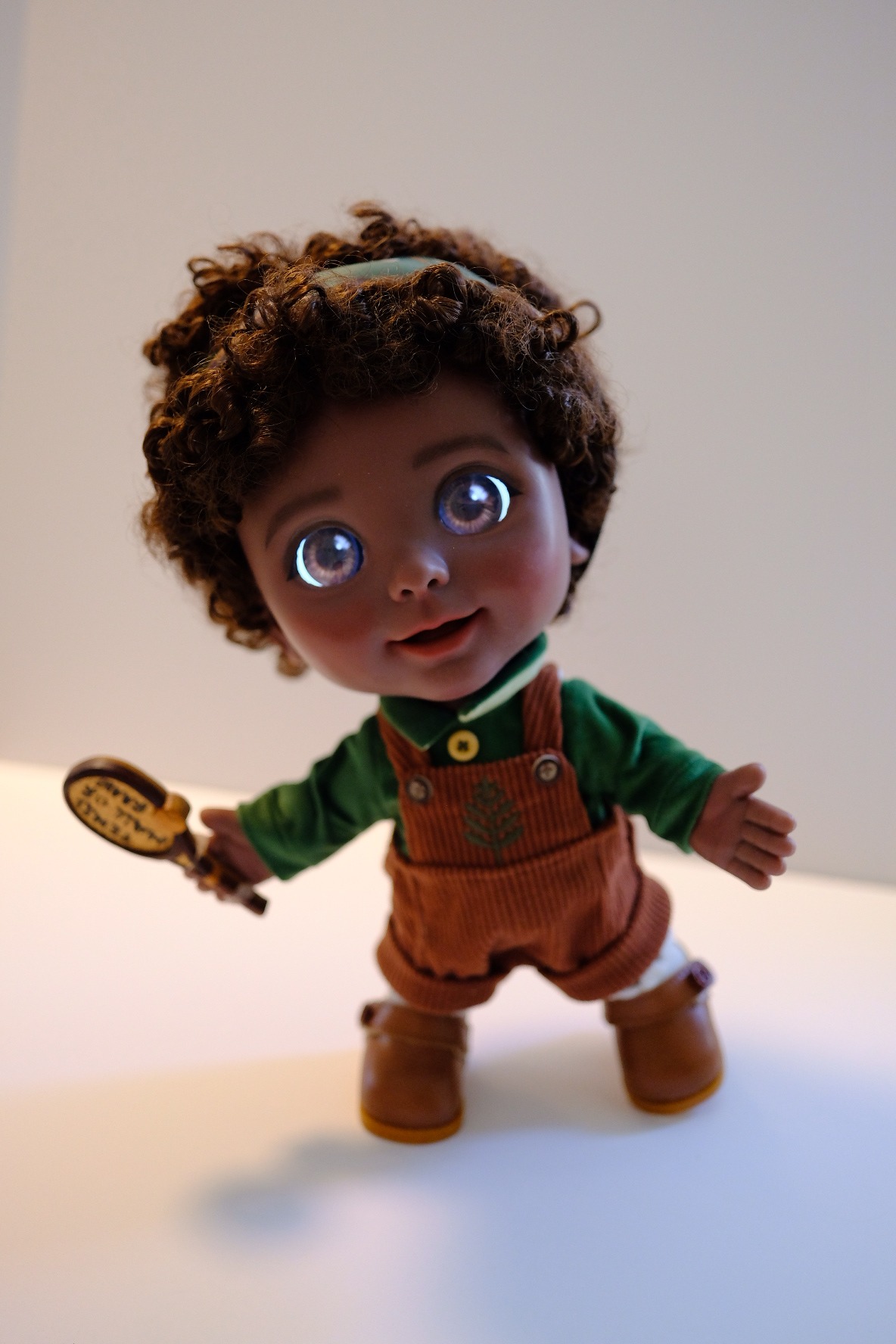 Joy with curly hair in the green velvet shirt and corduroy overalls, holding a small wooden paddle