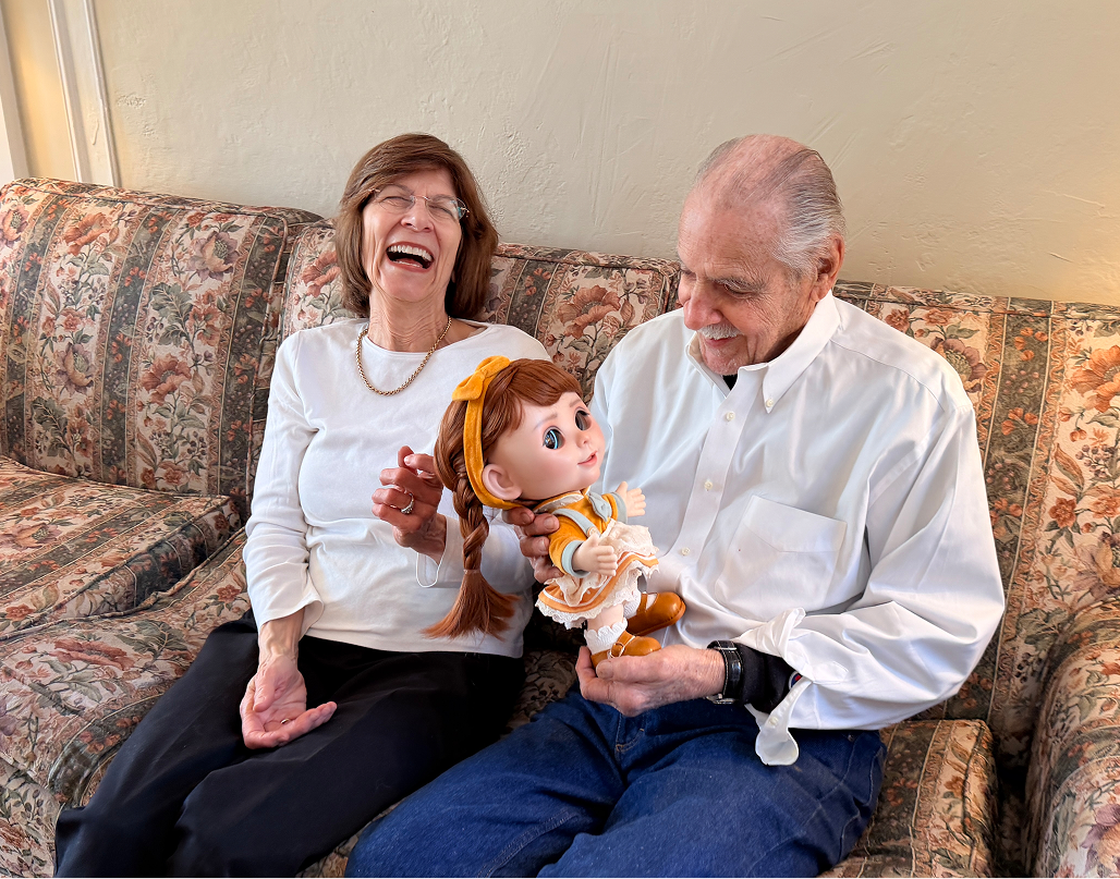 An older couple laughing together on the sofa with Joy