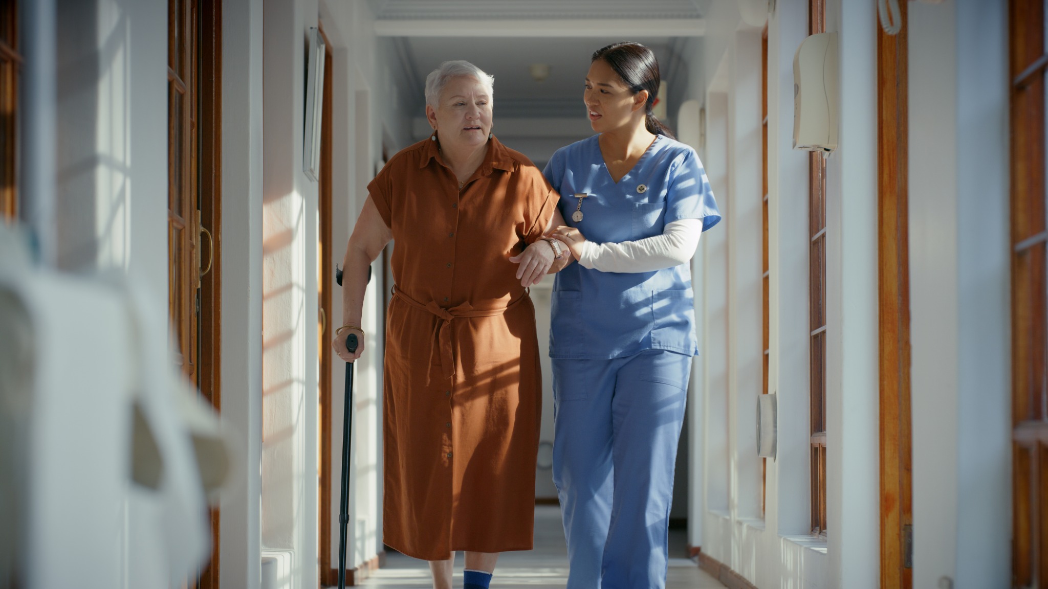 A healthcare professional supporting an older adult walking with a cane.