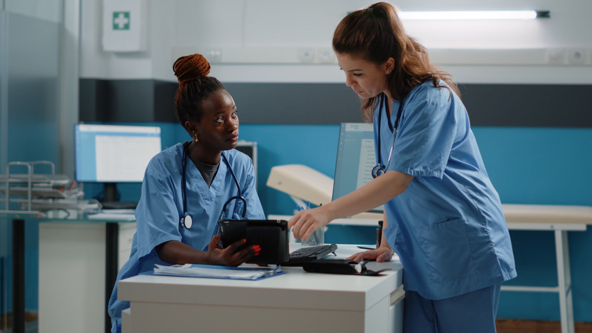 Two healthcare professionals in blue scrubs reviewing information on a tablet.