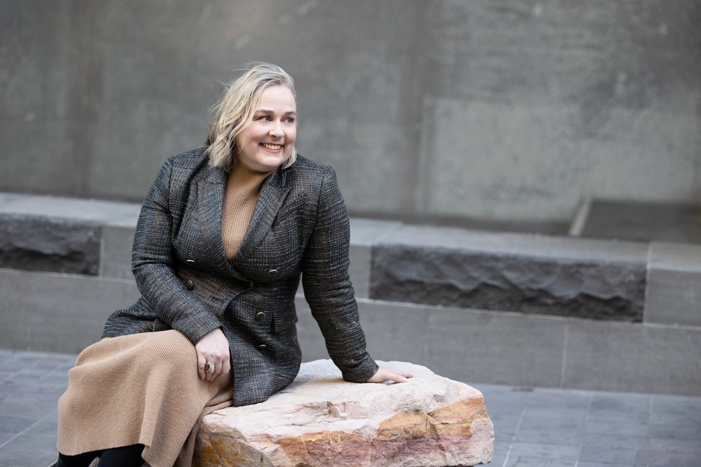 Catherine Hills smiling, seated on a sandstone block in a city laneway