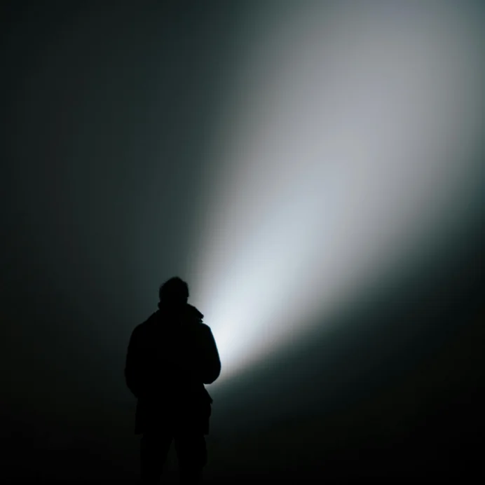A figure shining a torch beam into the dark