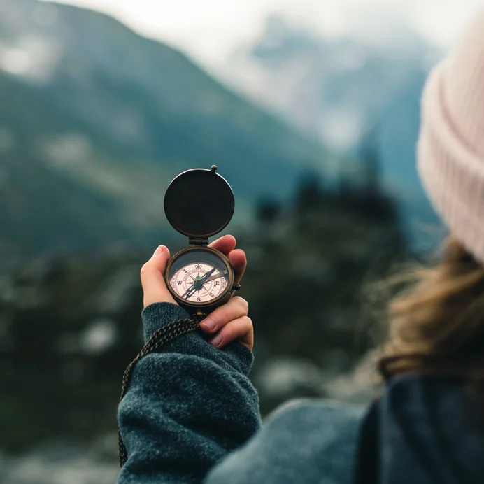 A hand holding a compass against a mountain landscape