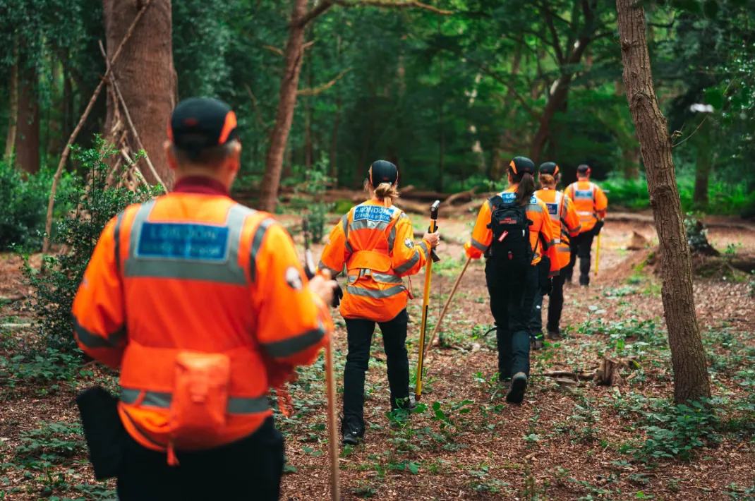 London Search and Rescue volunteers in high-visibility jackets walking through woodland