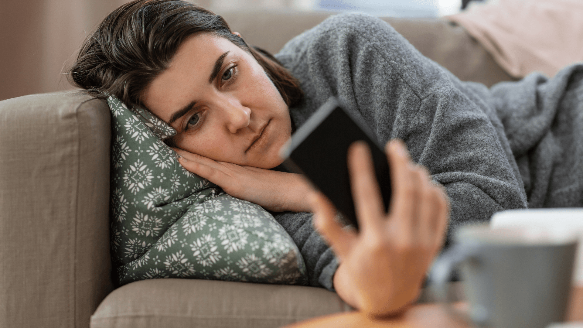 woman doomscrolling her phone while lying on a couch