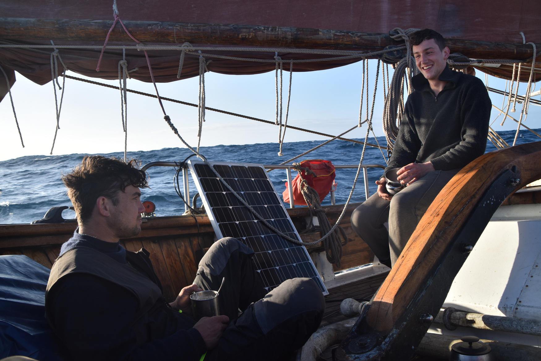 Two crew members fitting a solar panel on deck of a sailing ship