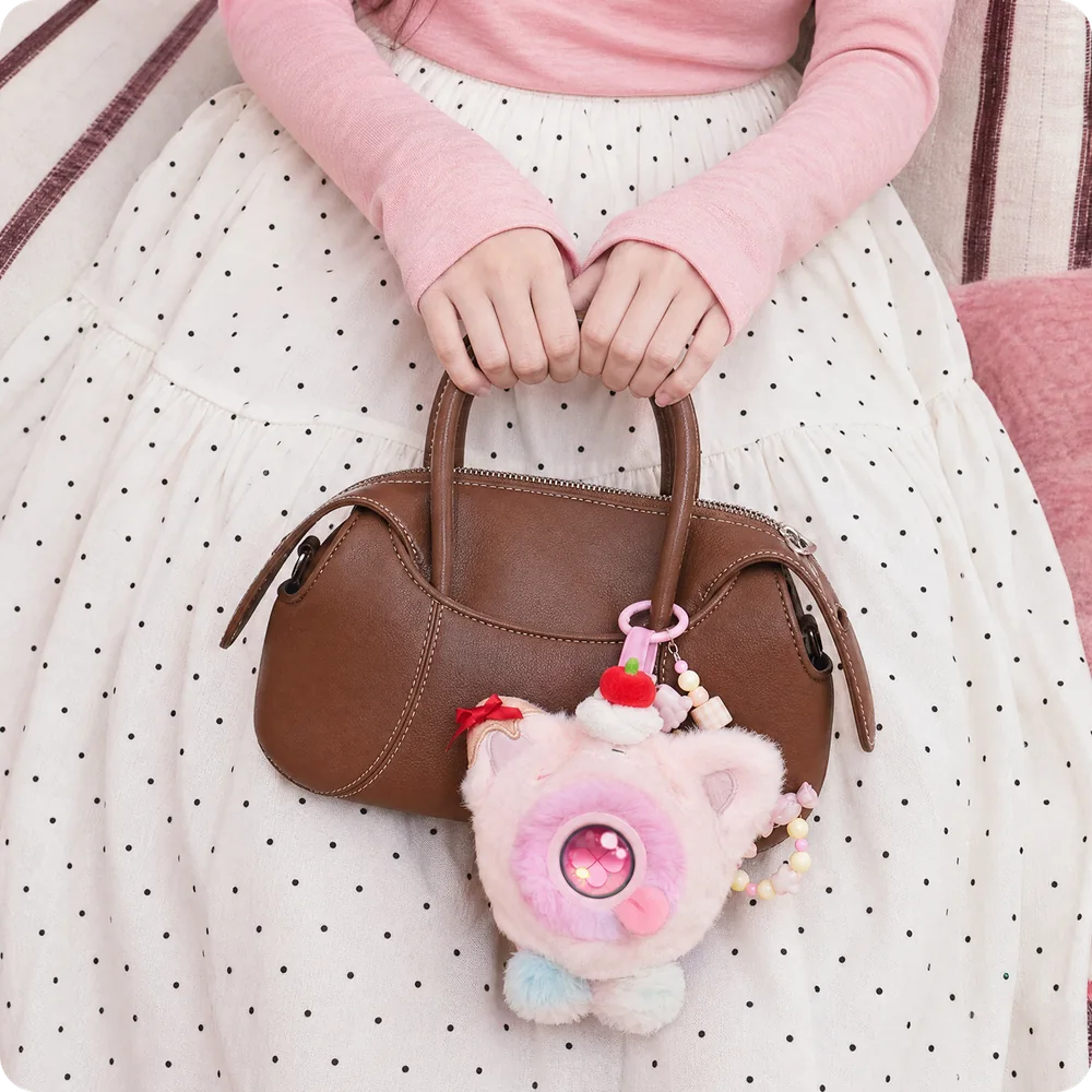 A pink Mumuland companion clipped to a brown handbag