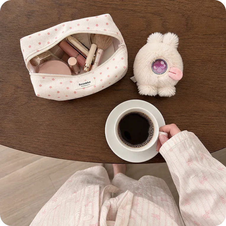 A coffee, a cosmetic pouch, and a Mumuland companion on a wooden table
