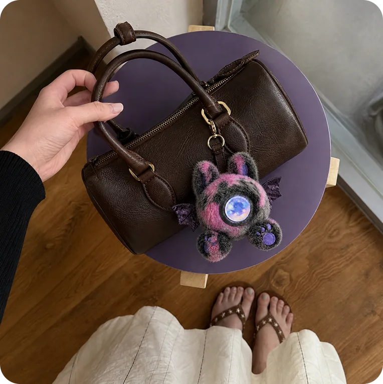 A dark Mumuland companion clipped to a brown handbag