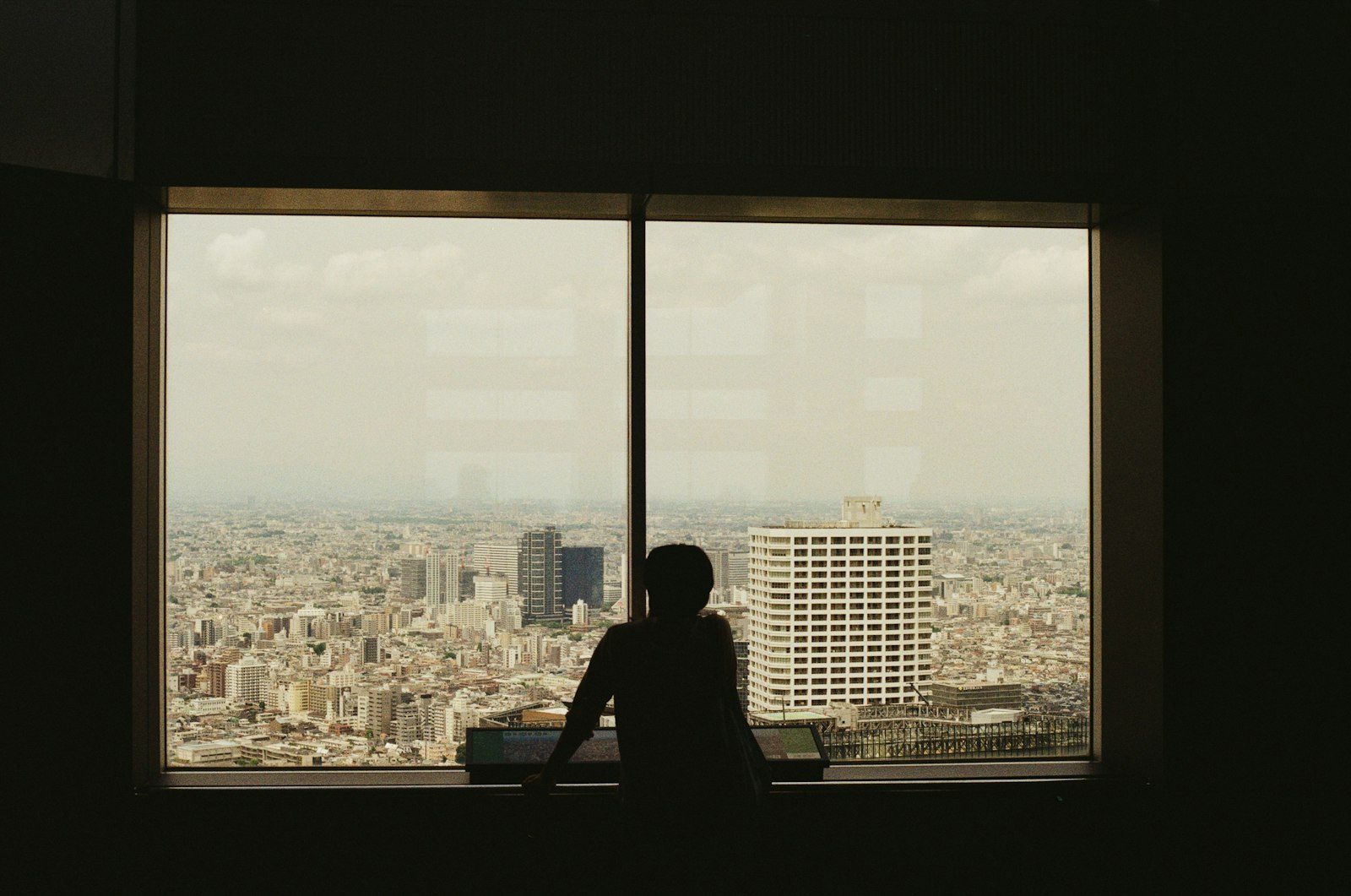A silhouette of a person looking out over a city through a window