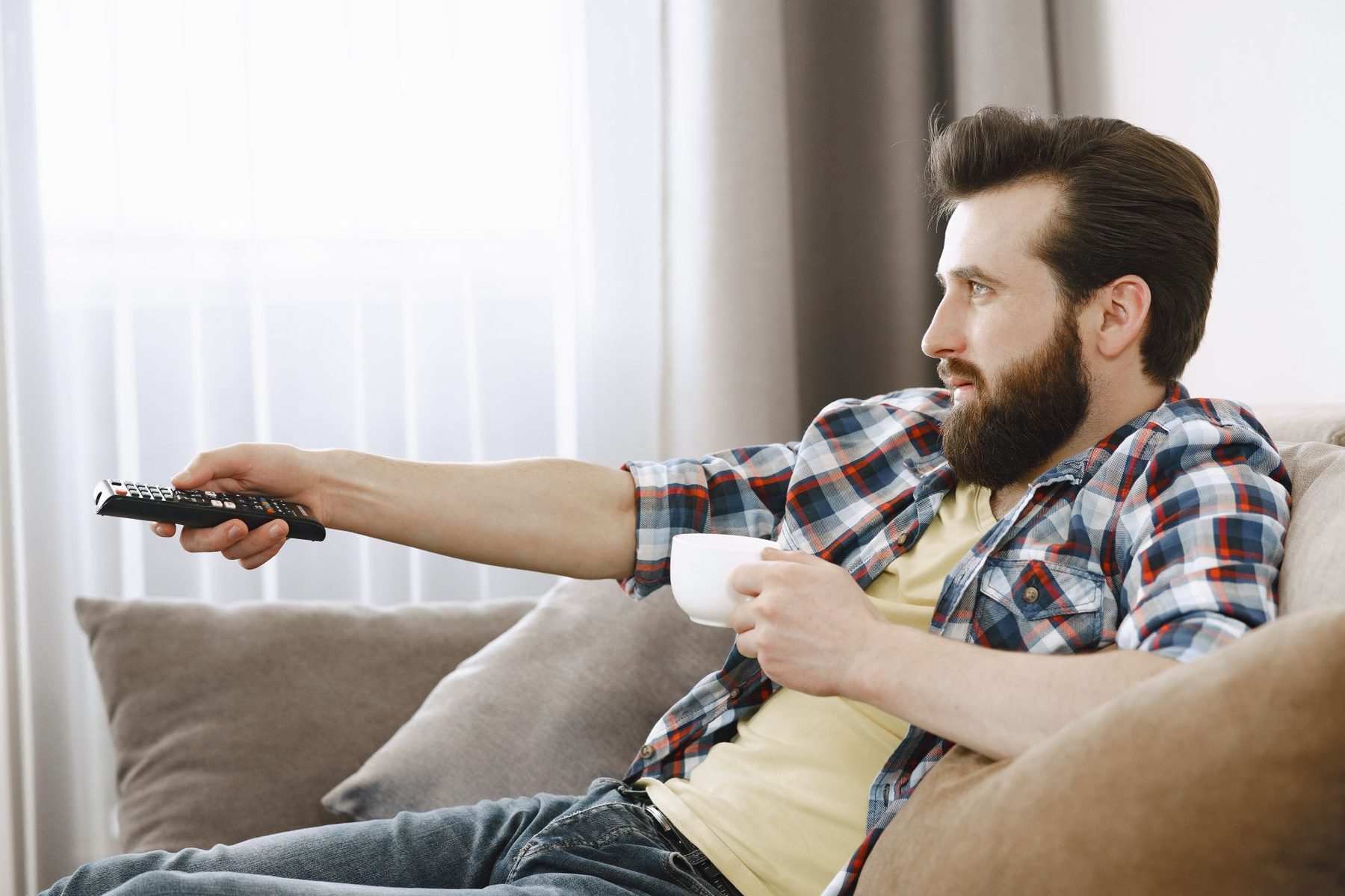 Man relaxing on a sofa pointing a remote at a television