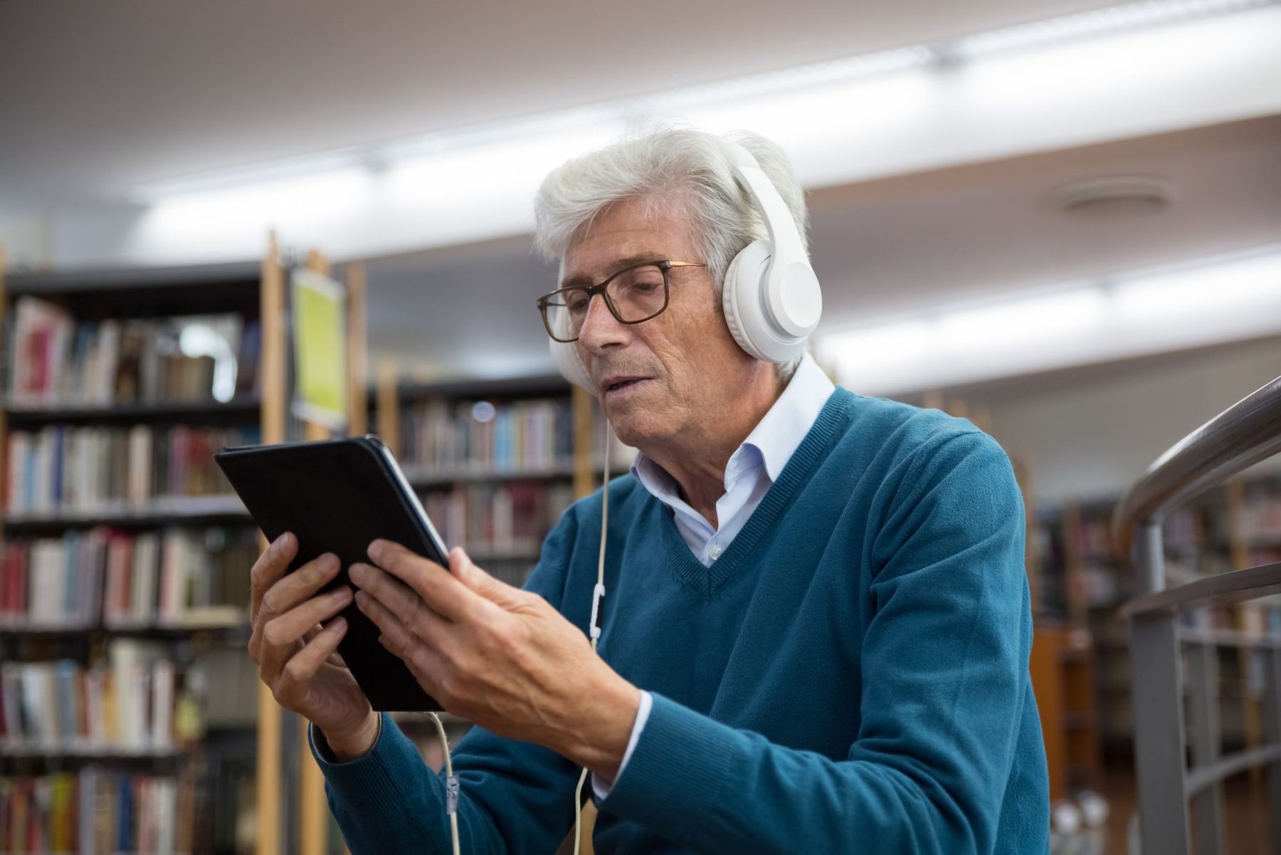 Older man wearing headphones watching a video on a tablet in a library