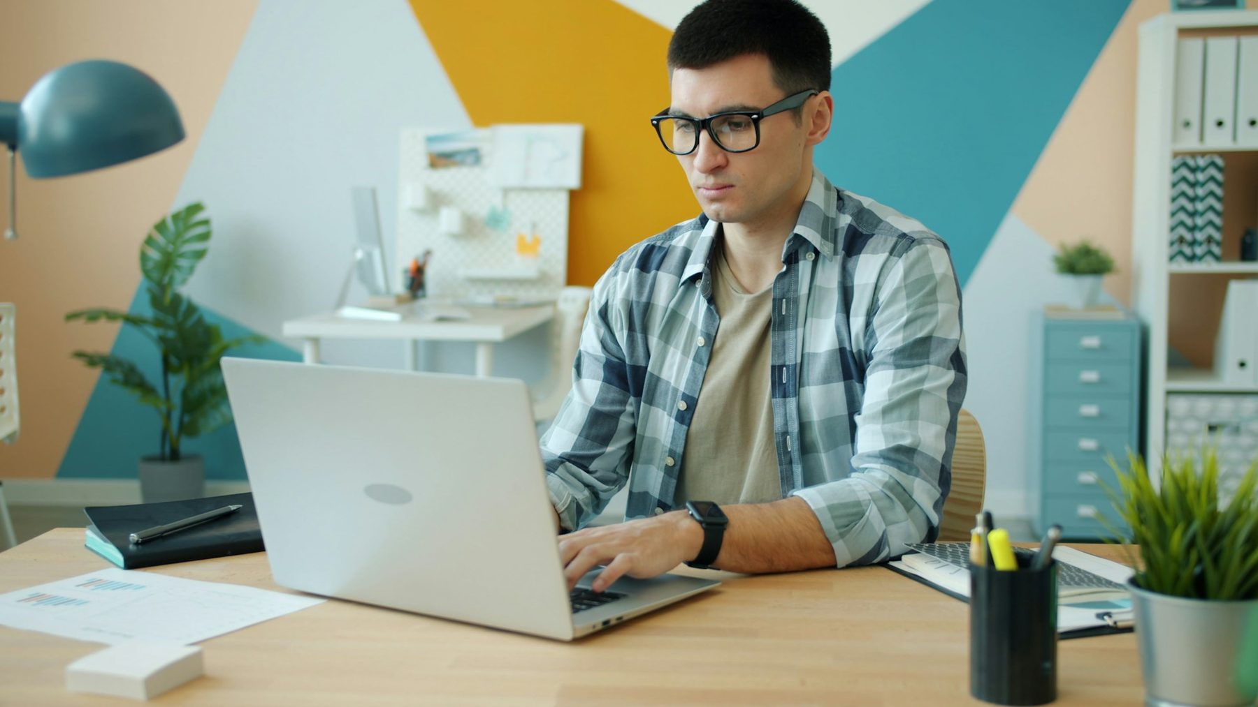 Man in glasses typing title options on a laptop in a bright home office