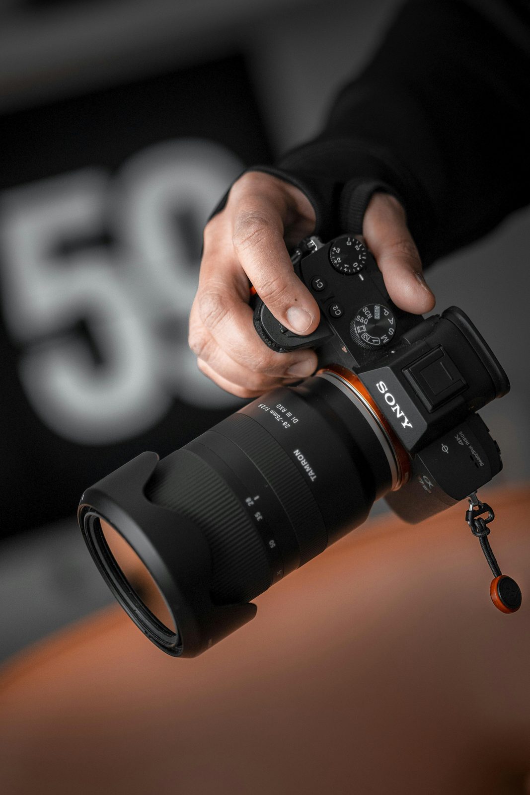 Hands gripping a Sony Alpha camera with a zoom lens