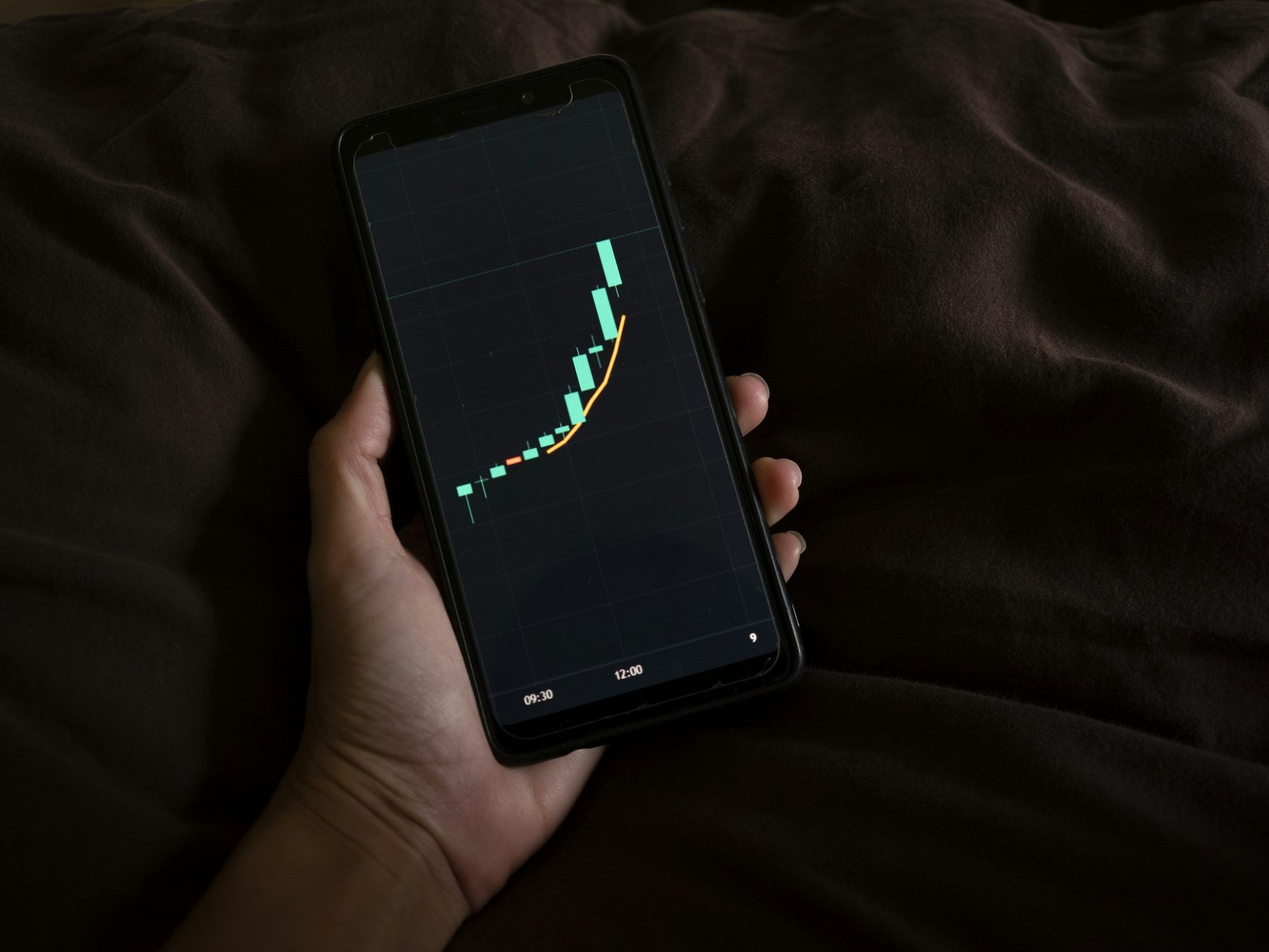 Hand holding a smartphone showing a rising line and bar chart