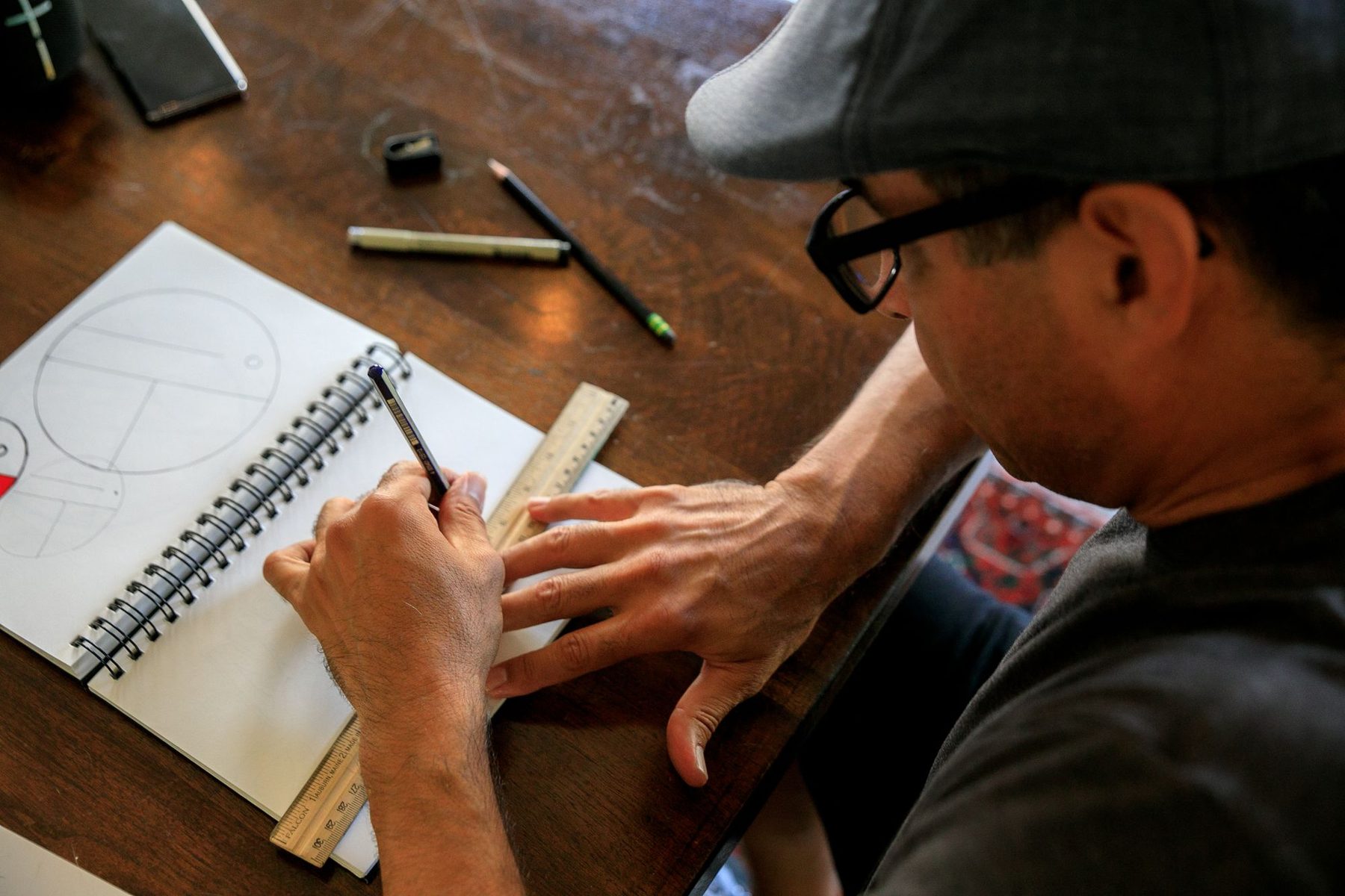 Designer in glasses sketching thumbnail layout ideas in a notebook with a ruler and pens
