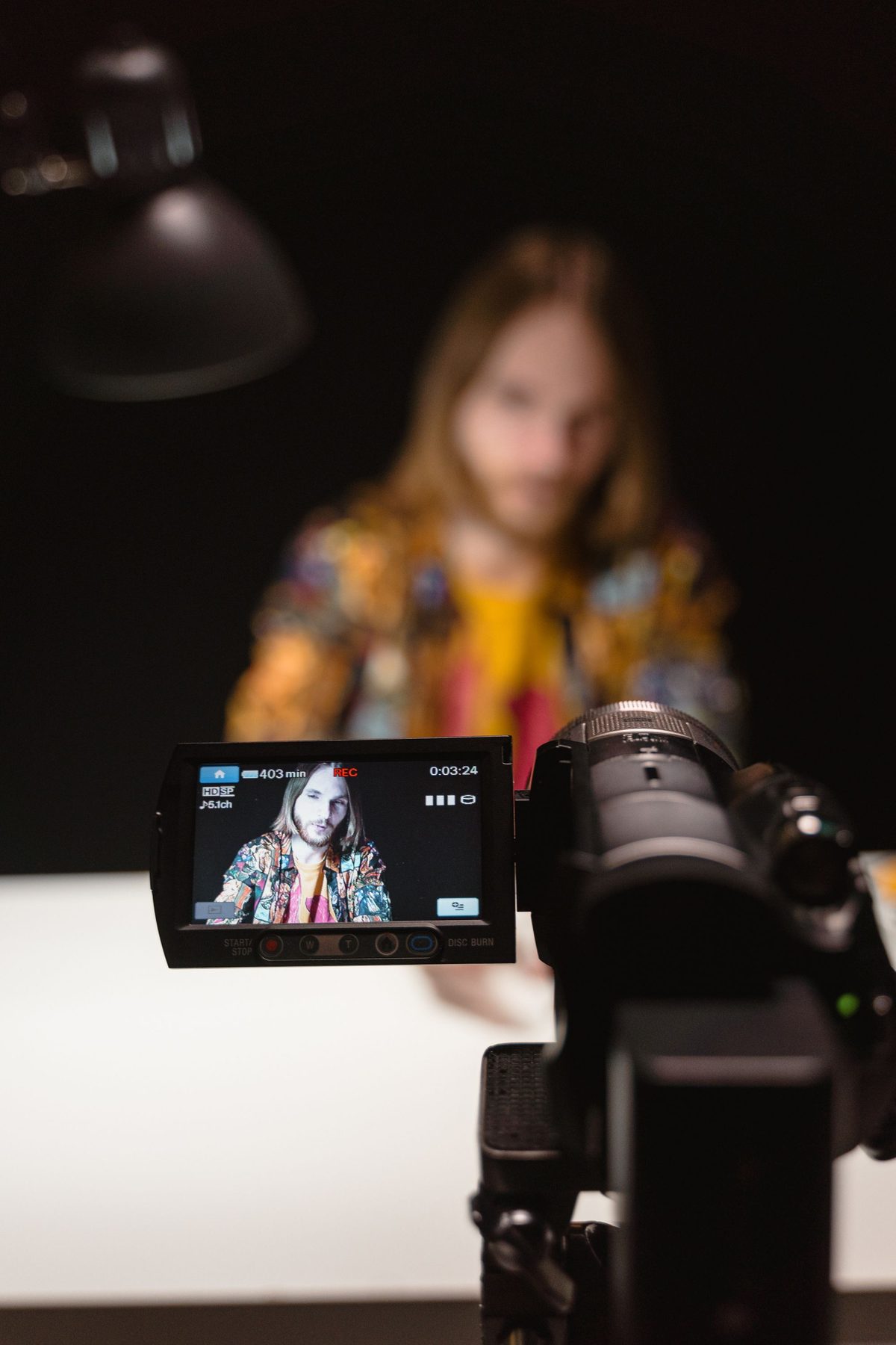 Camcorder flip screen recording a presenter talking to camera in a dark studio