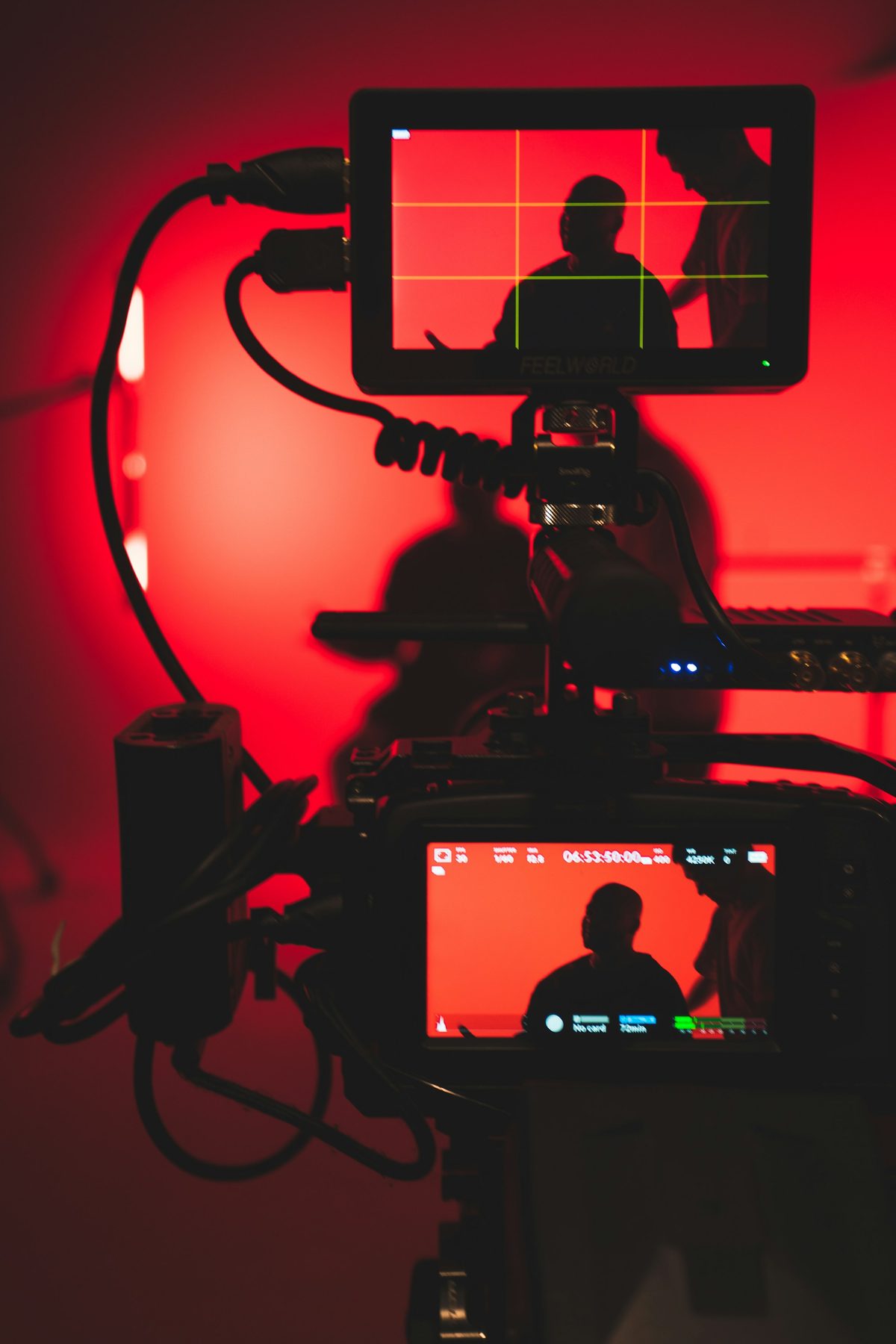Cinema camera rig with monitors silhouetted against a red studio background before a take