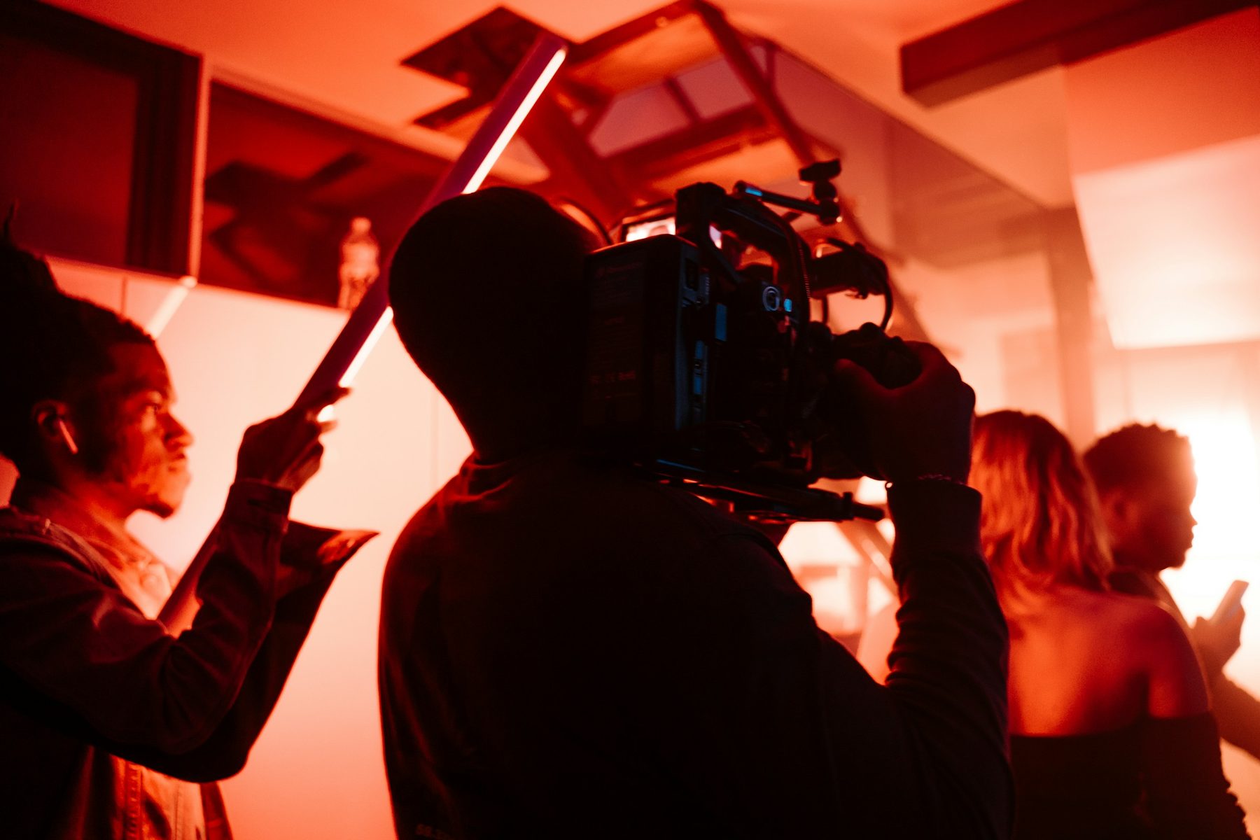 Camera operator filming in a studio flooded with red light with crew around