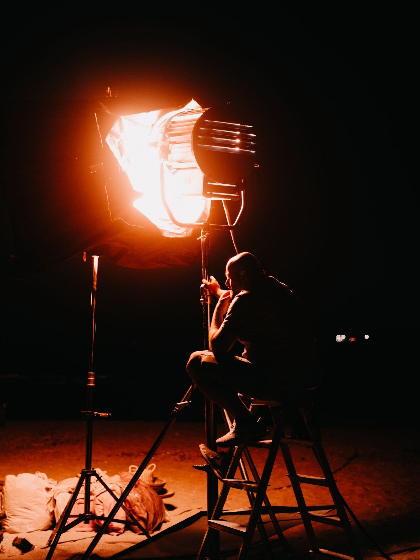 Silhouetted crew member beside a blazing orange red studio lamp in a dark studio