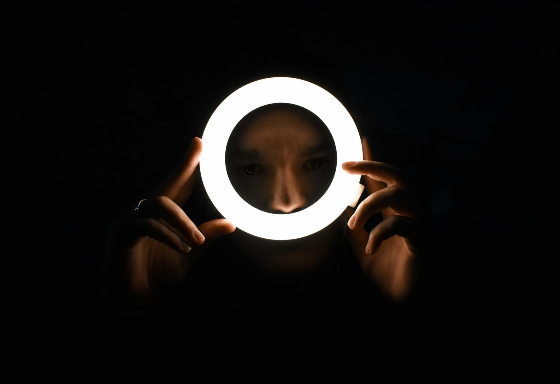 Person holding a glowing ring light in a dark room