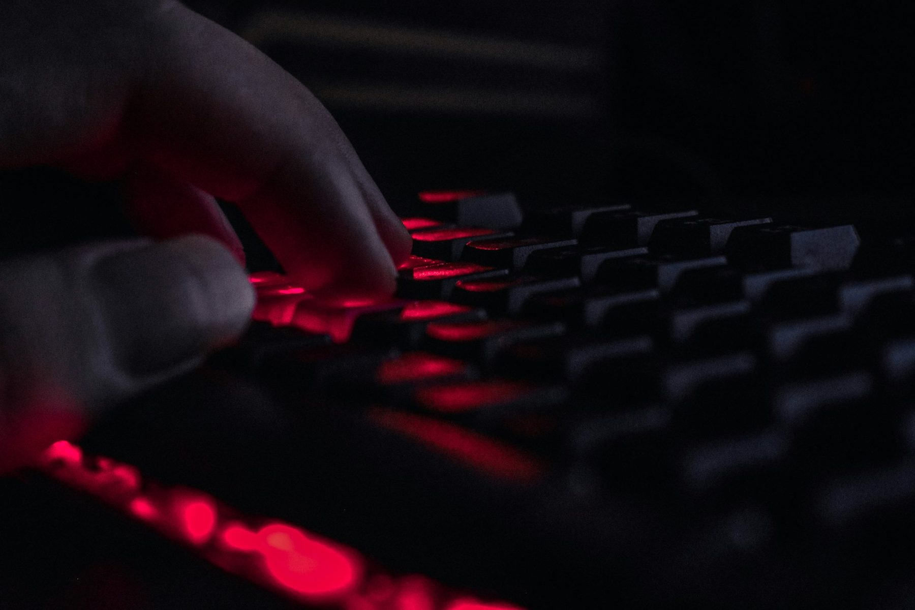Fingers typing on a keyboard lit by red key glow in a dark room