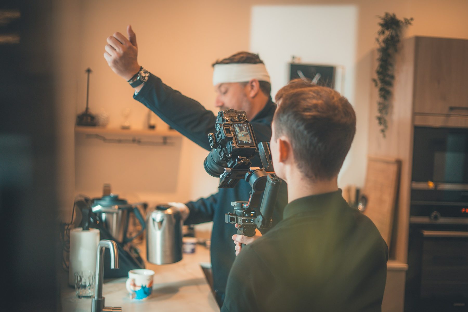 Content creator with a gimbal filming a man preparing food at a home kitchen counter