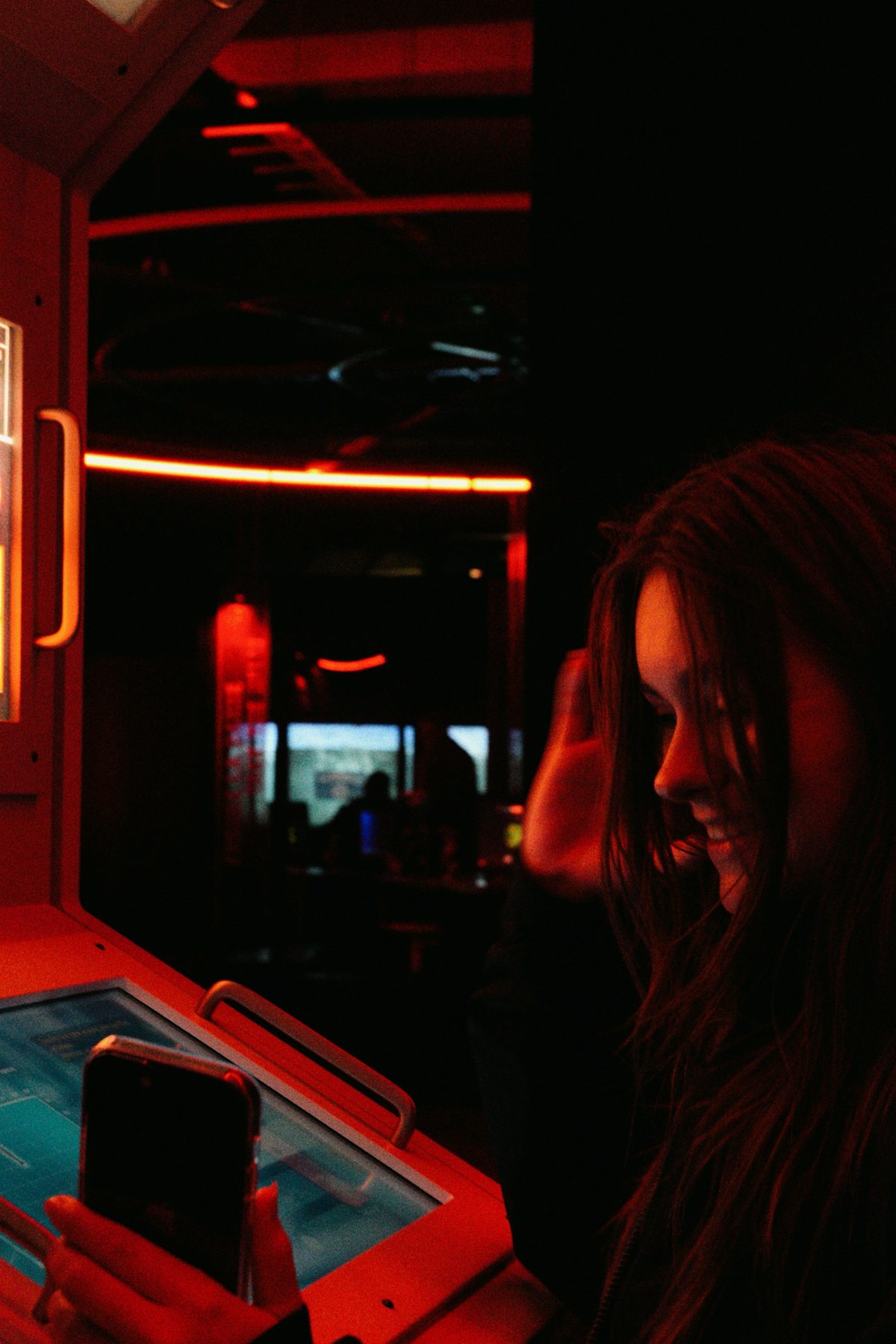 Young woman holding a phone in a dark space lit by red neon