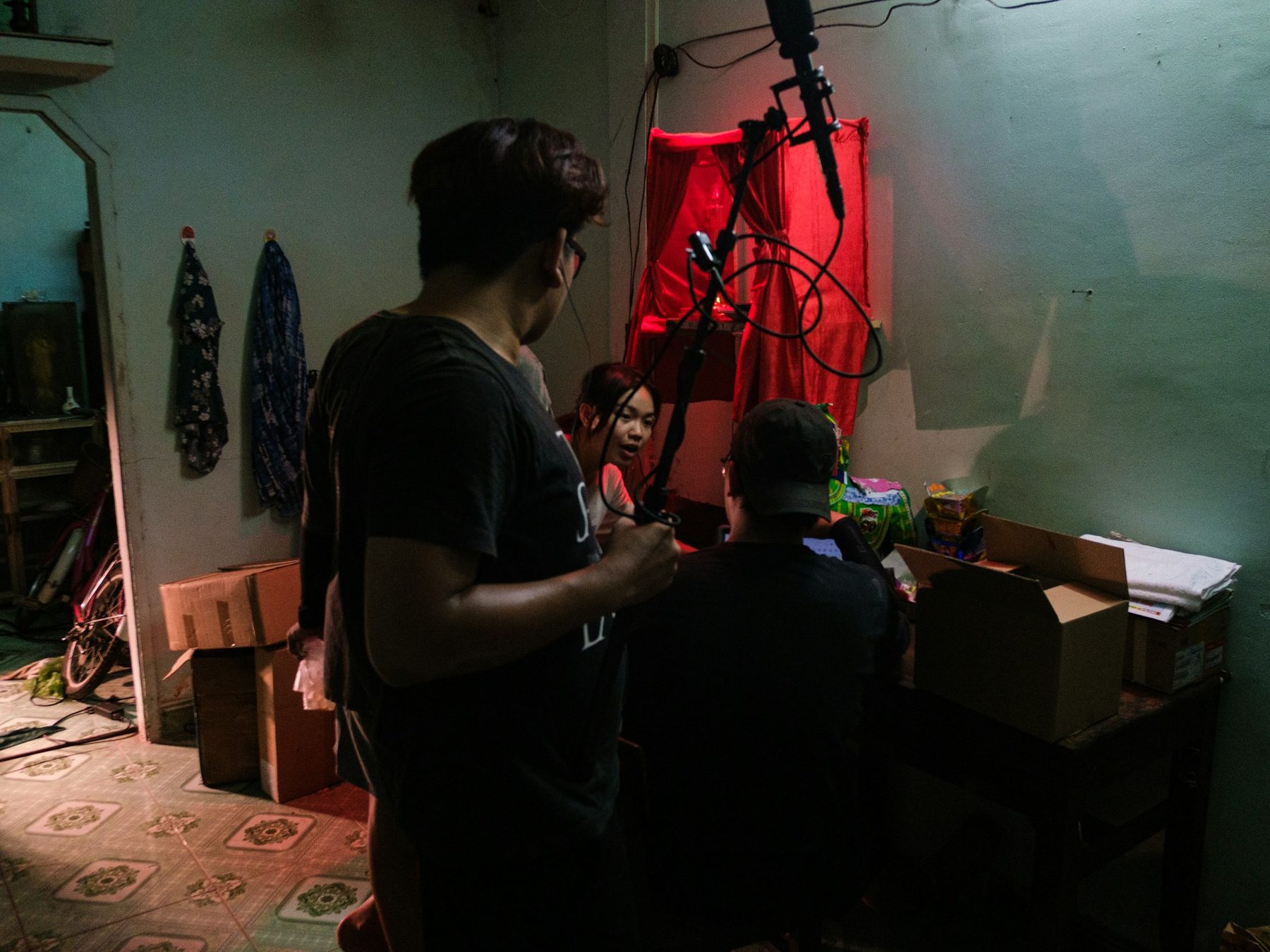Documentary crew recording an interview in a dim room lit with a red curtain and boom microphone