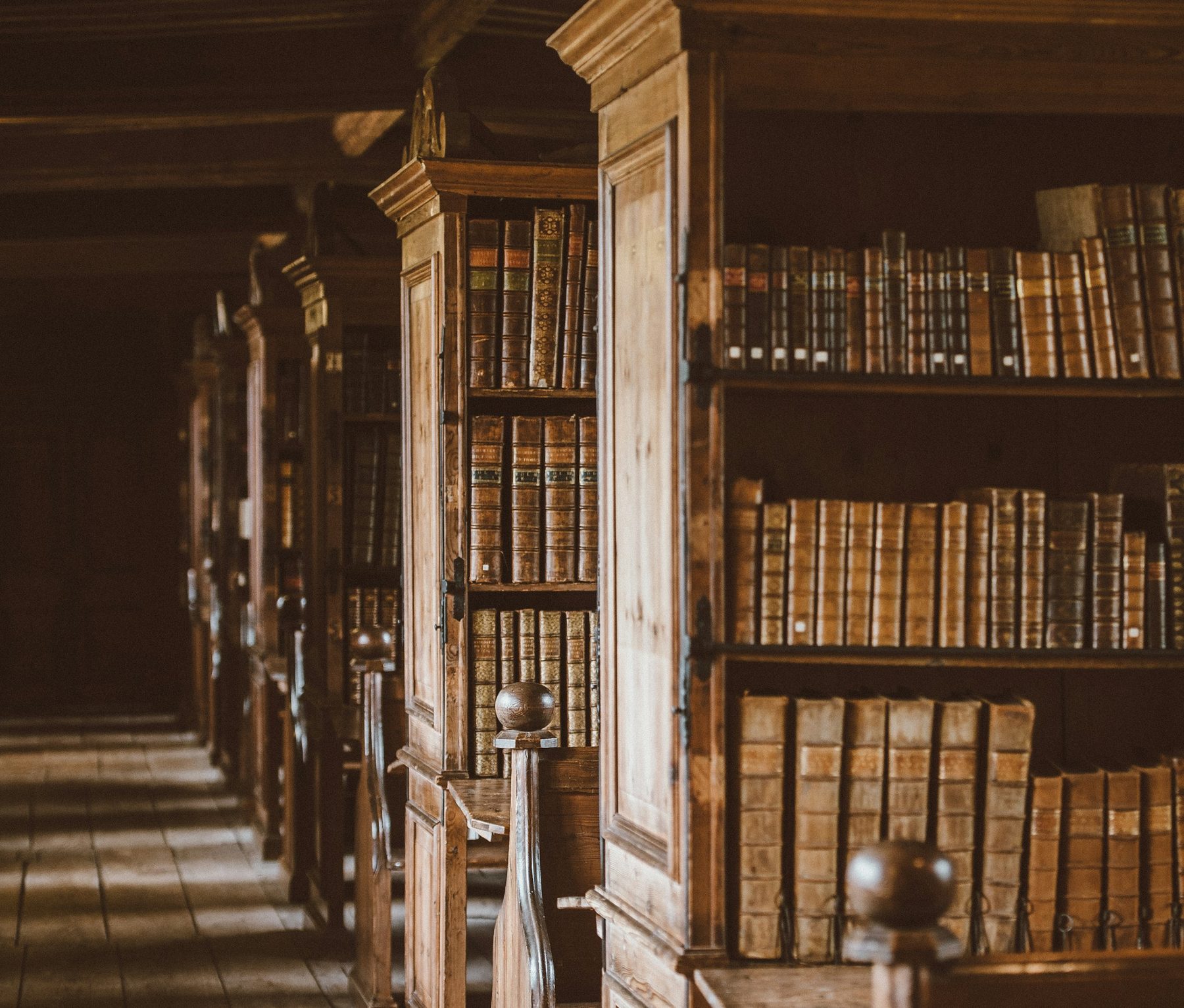 Rows of old leather bound books on wooden library shelves in warm low light