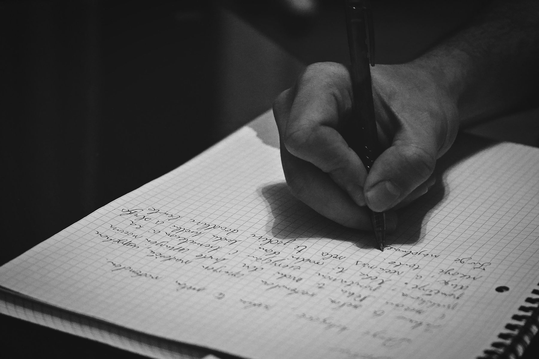Black and white close up of a hand writing in a squared paper notebook