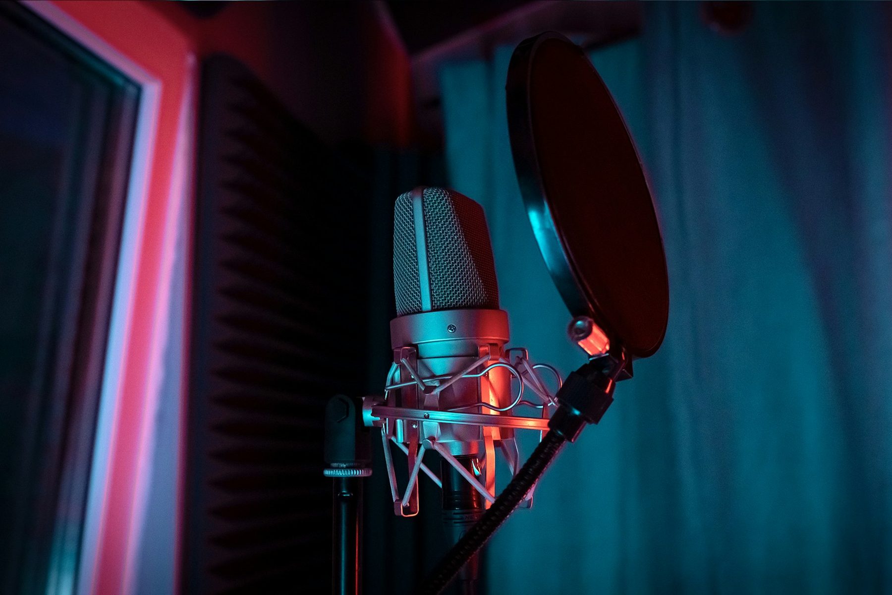Studio condenser microphone with pop filter in a recording booth lit red and teal