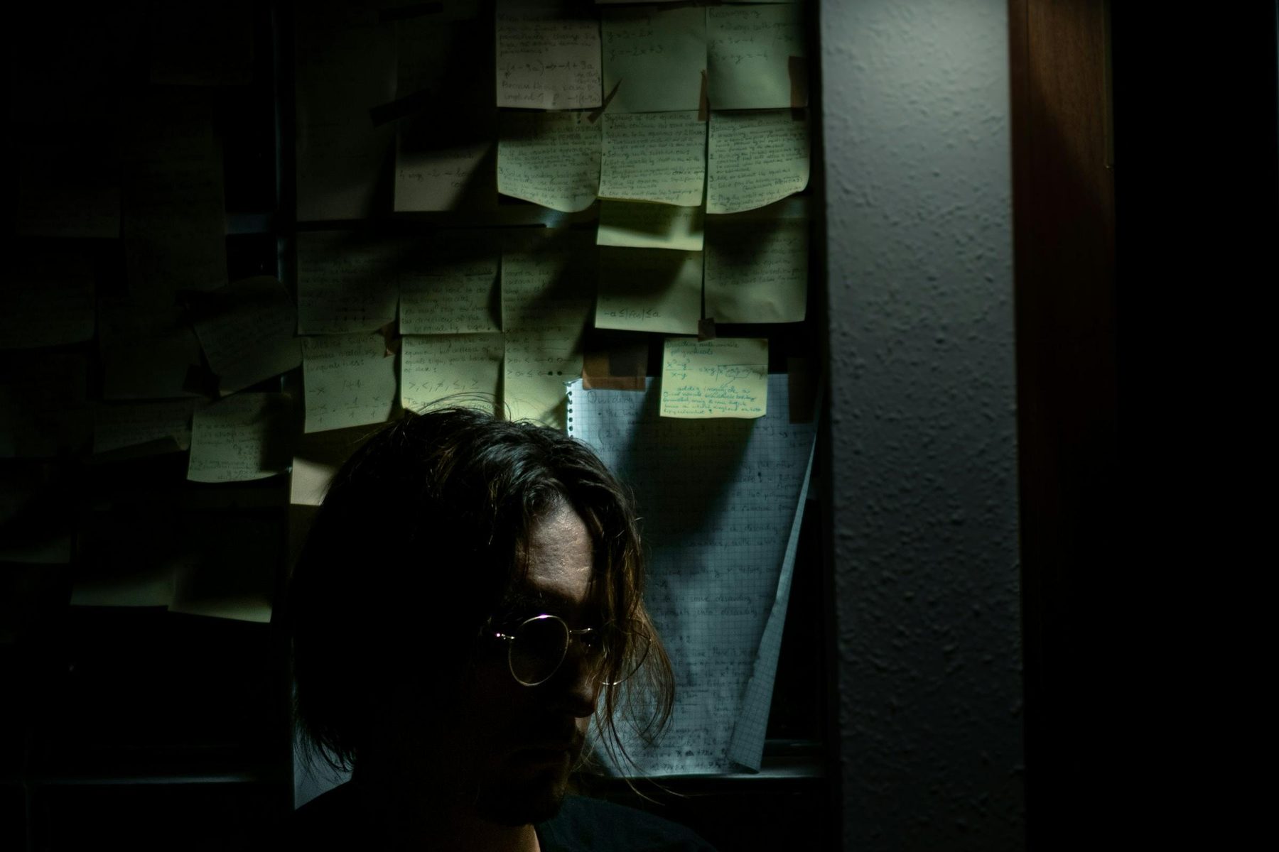 Wall of sticky notes in a dark planning room with a person thinking
