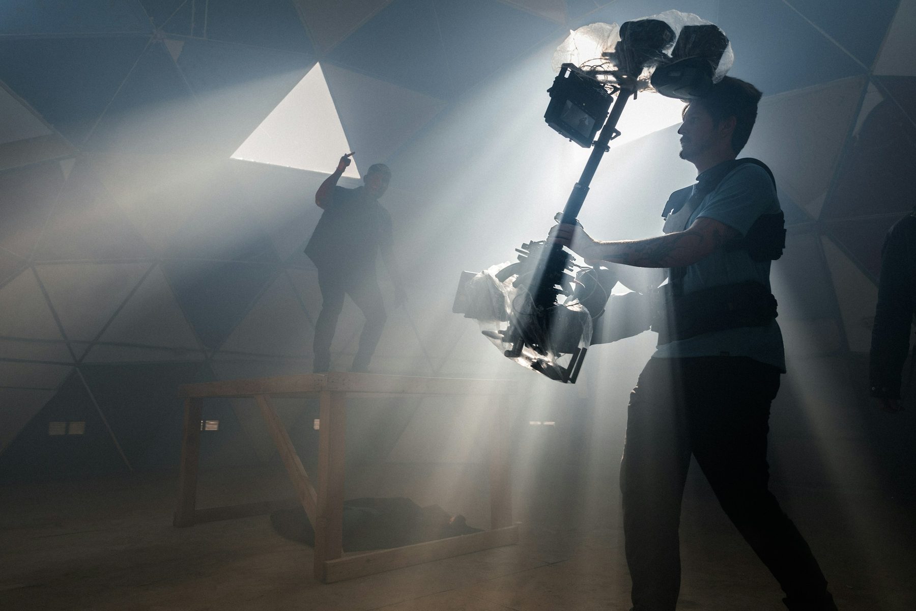 Camera operator carrying a stabilised rig through shafts of studio light