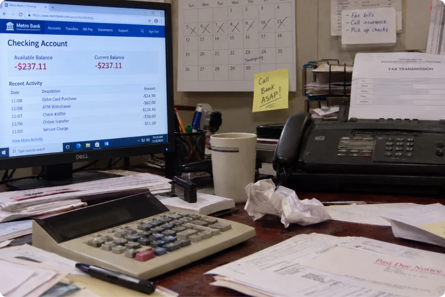 Cluttered office desk with a bank balance on screen, a calculator and a fax machine