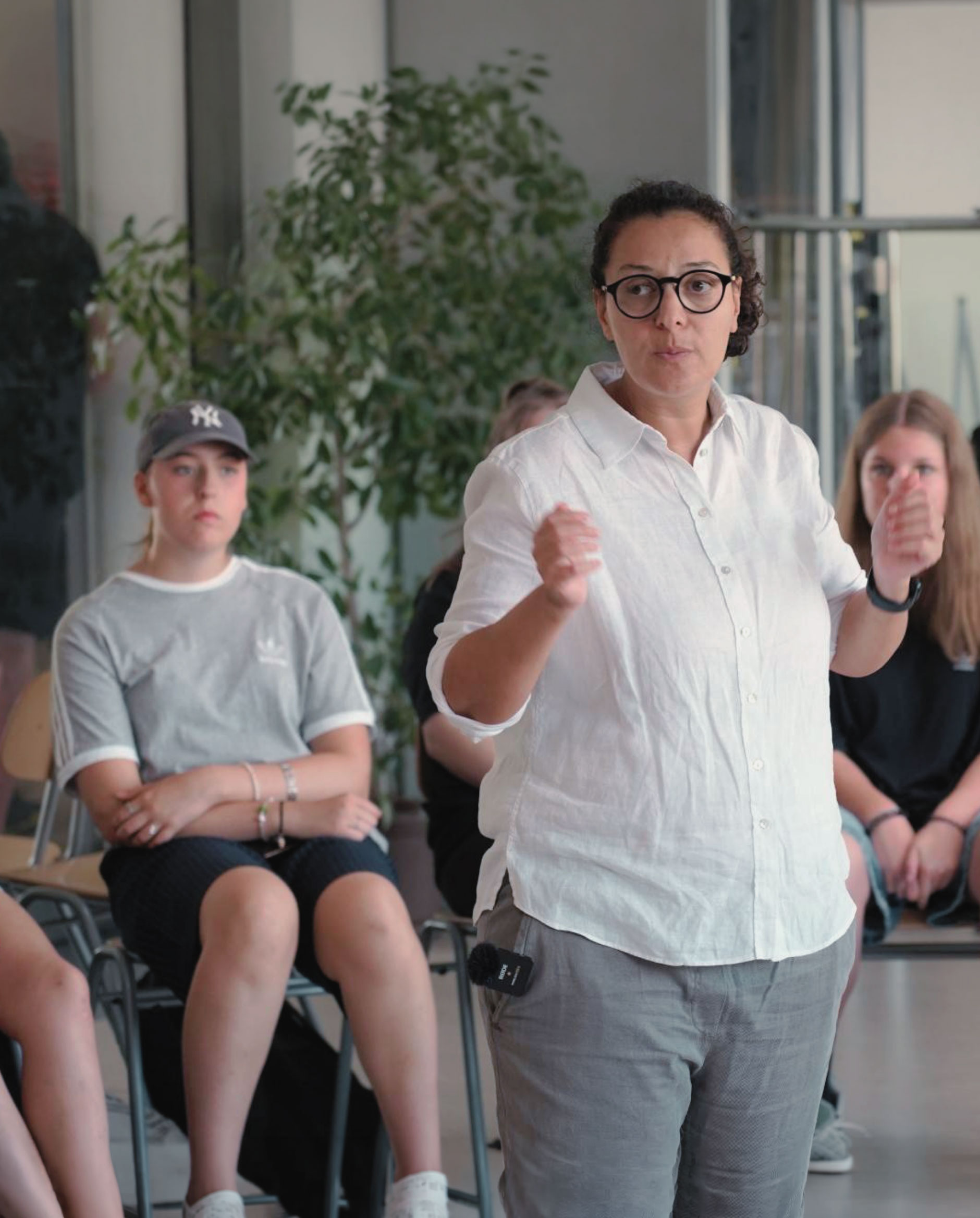 Eine Frau spricht engagiert vor einer Gruppe junger Menschen in einem Workshop.