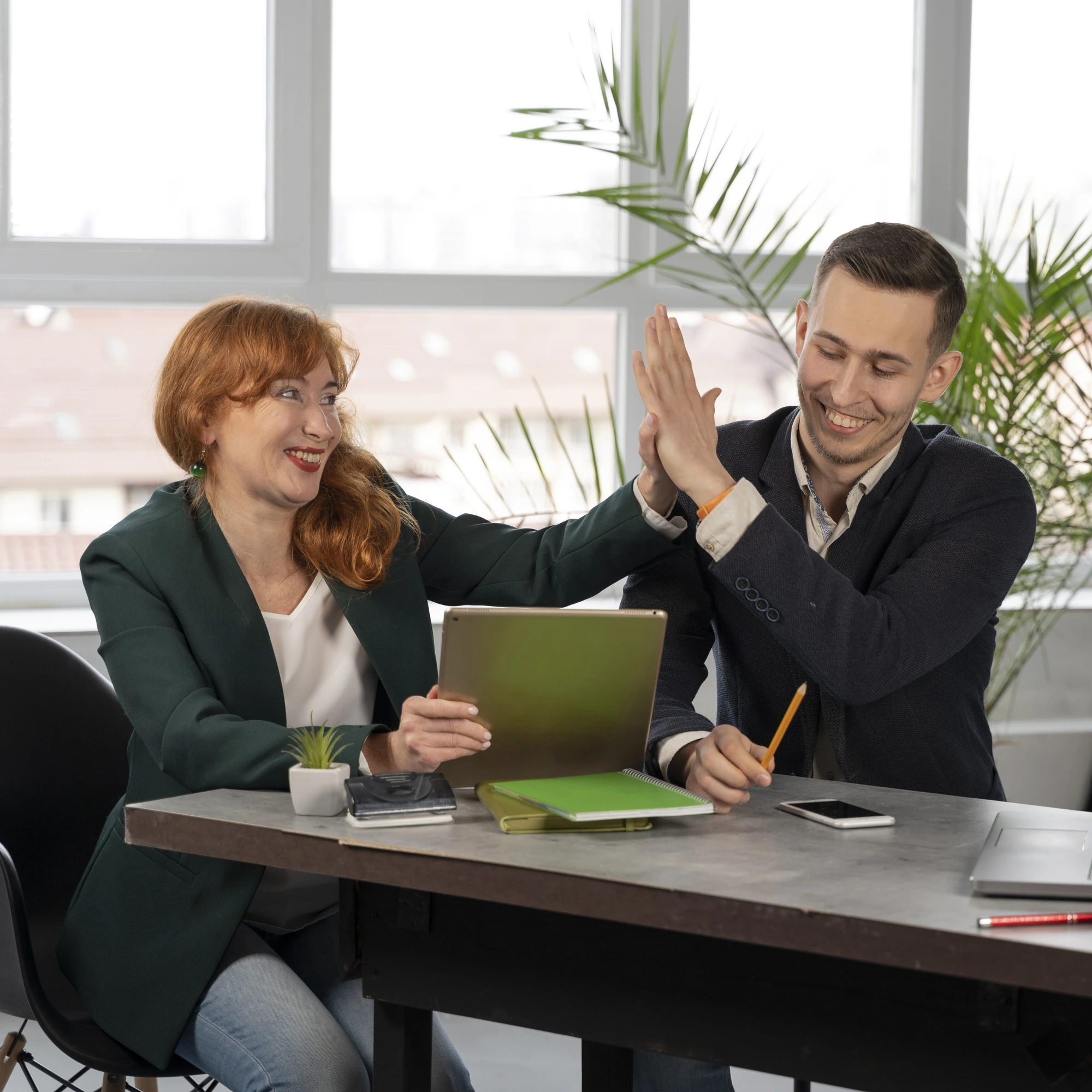 Two smiling coworkers high-fiving at a desk