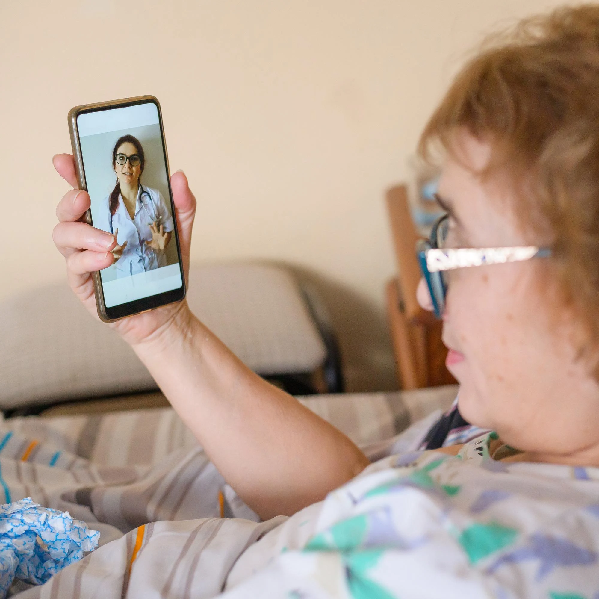 Woman in bed holding a smartphone video call with a female doctor