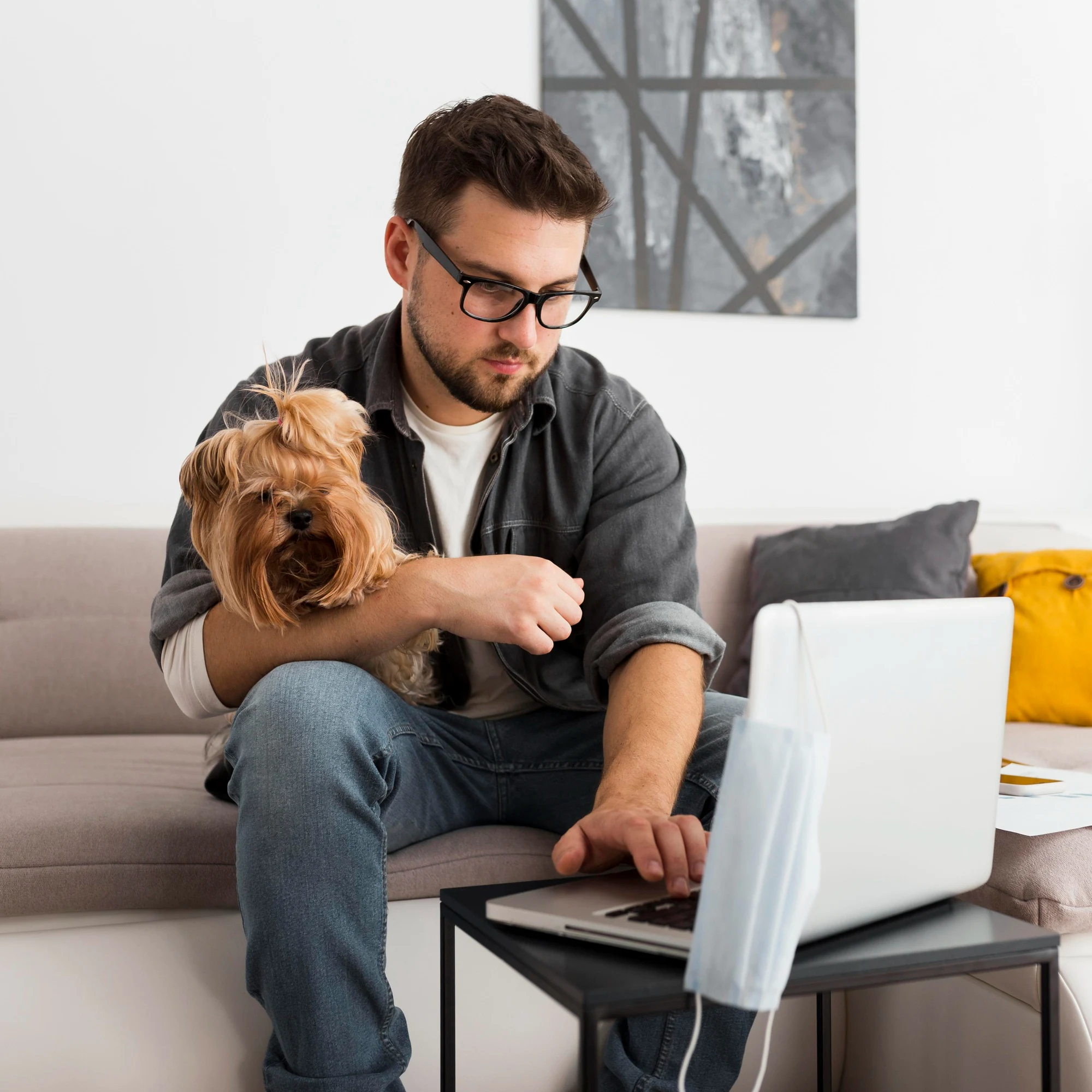 Man with a small dog on his lap using a laptop at home