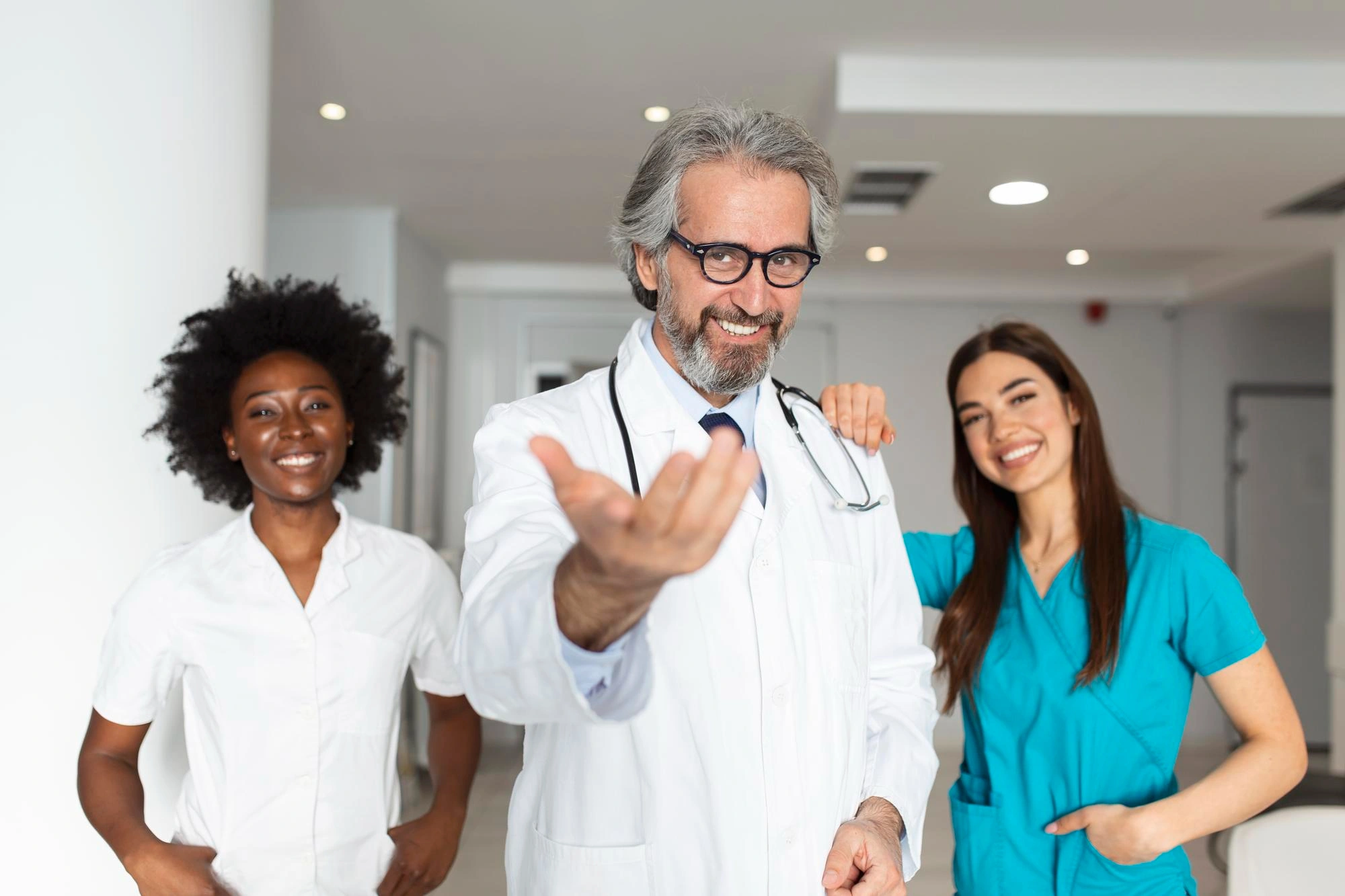 Three smiling healthcare professionals welcoming patients in a clinic