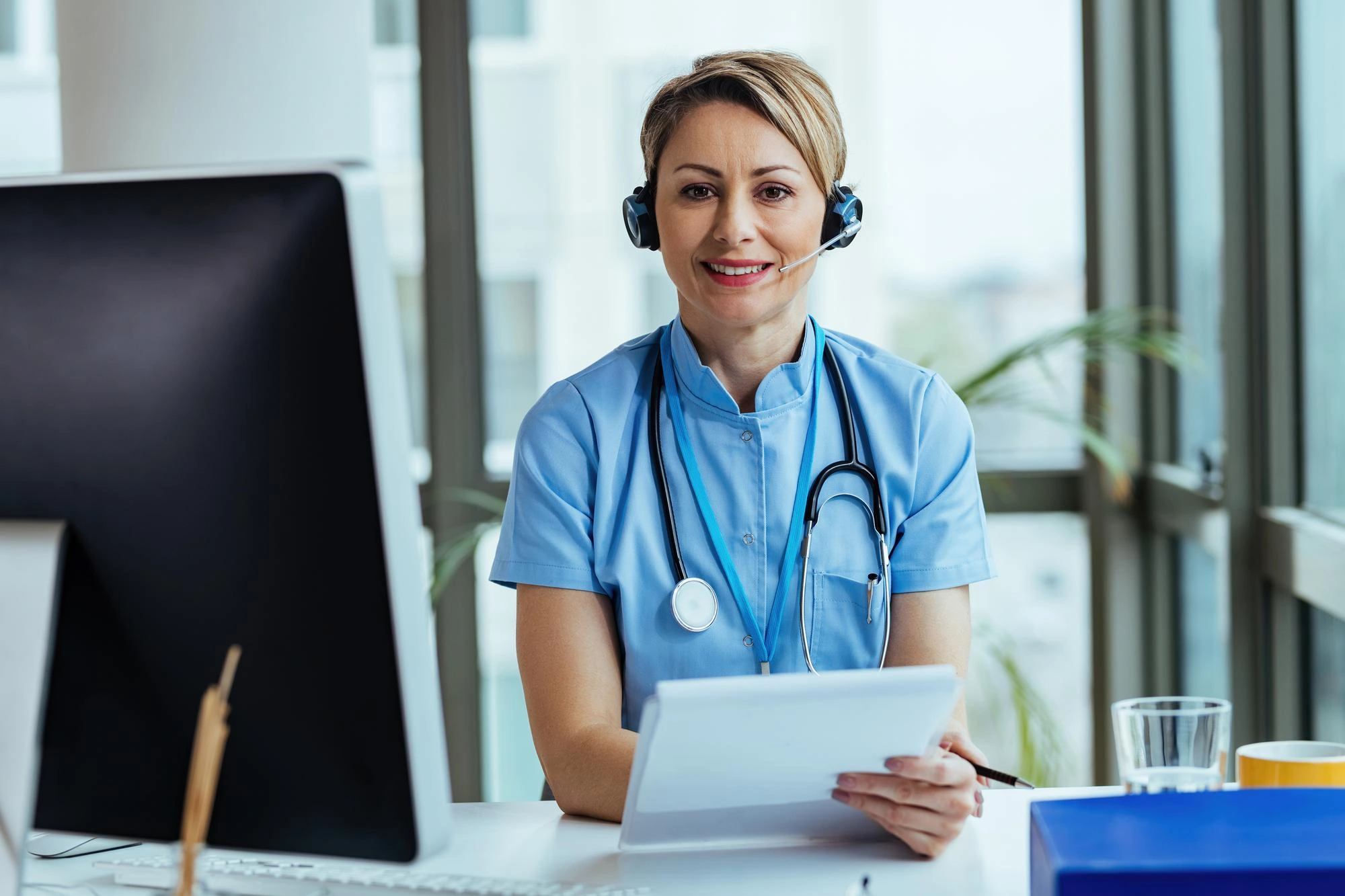 Smiling support representative wearing a headset and stethoscope at her desk