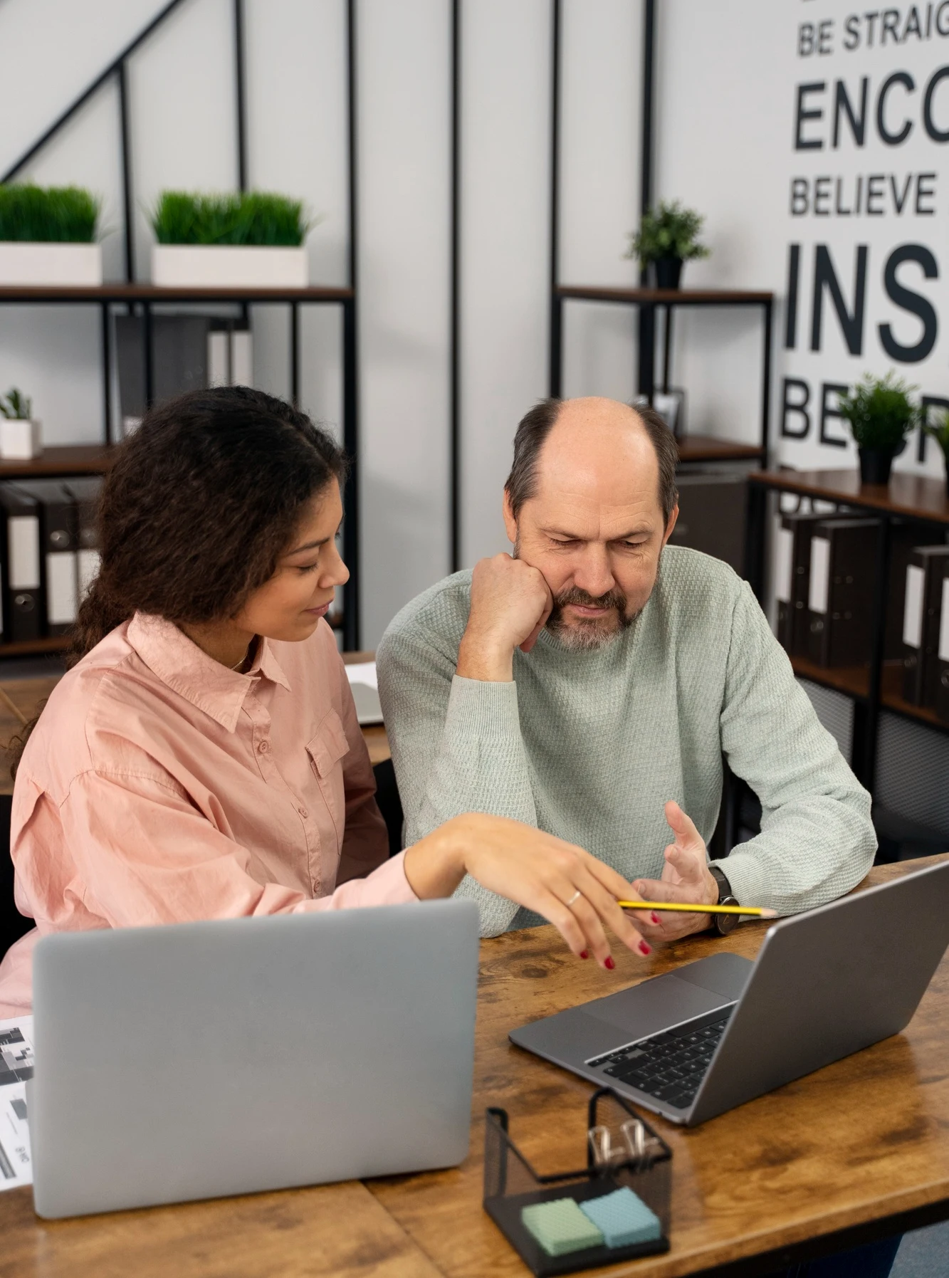 Two colleagues reviewing documents together at a desk with laptops