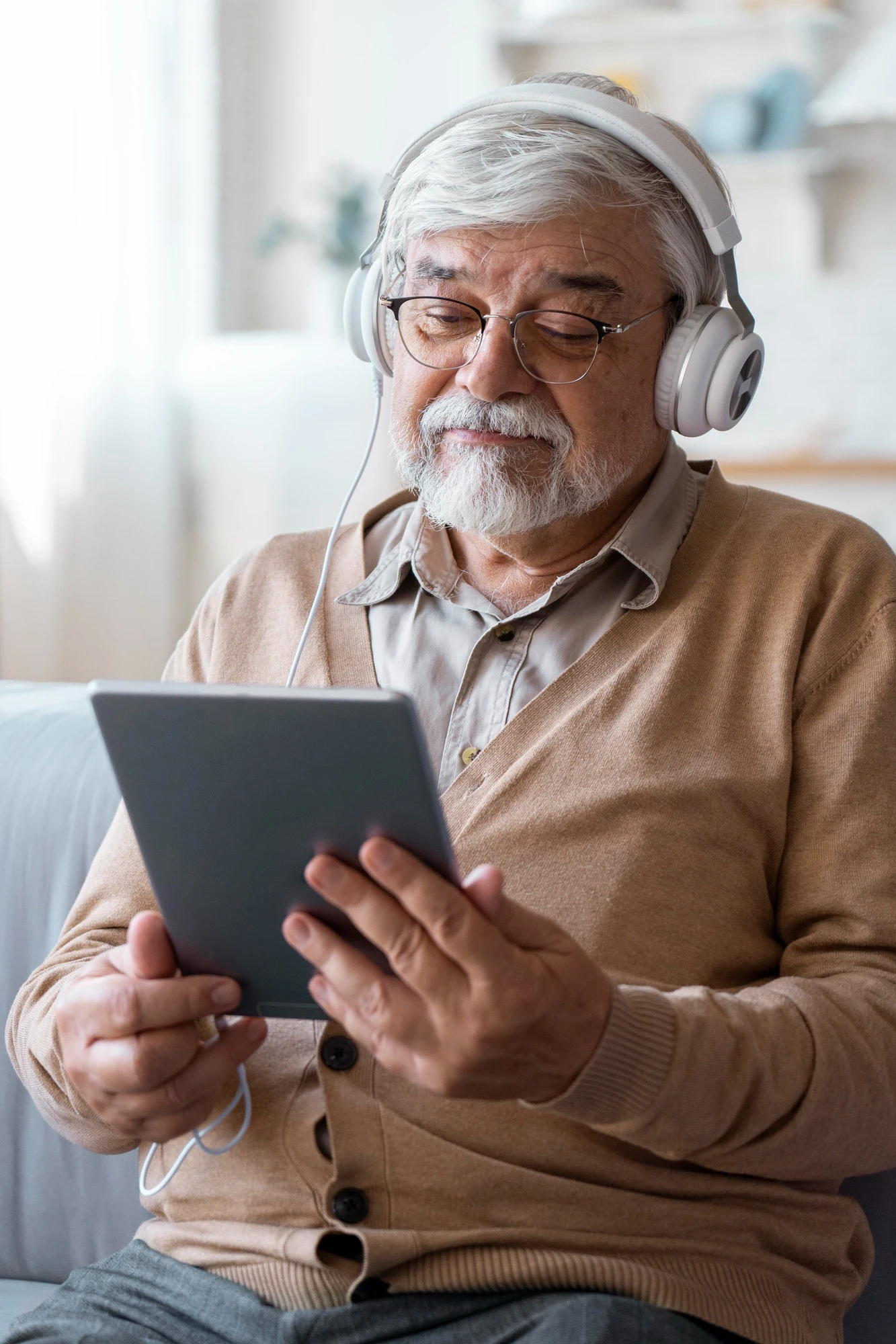 Senior man wearing headphones and glasses using a tablet at home