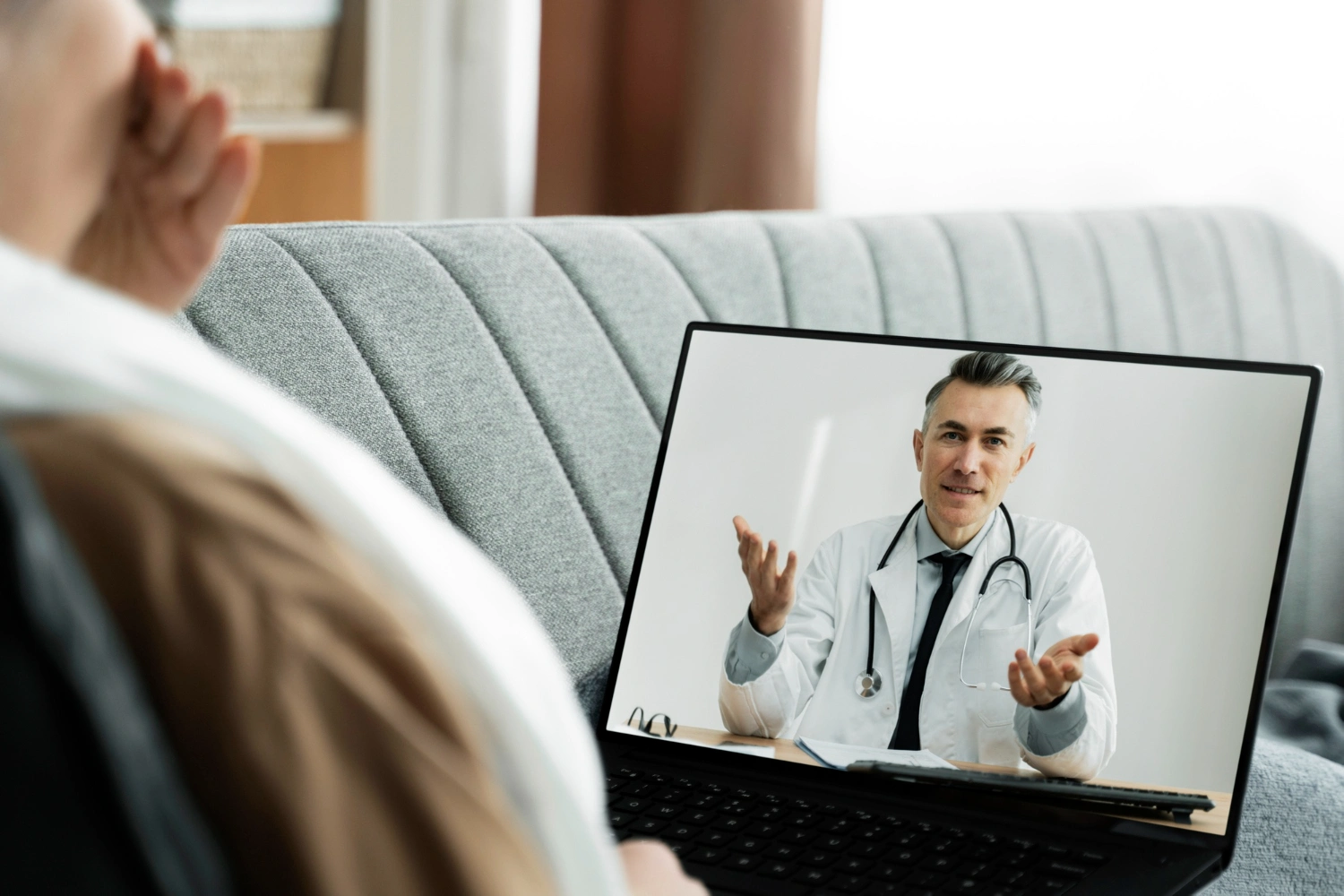 Doctor in a white coat speaking to a patient during a laptop video consultation