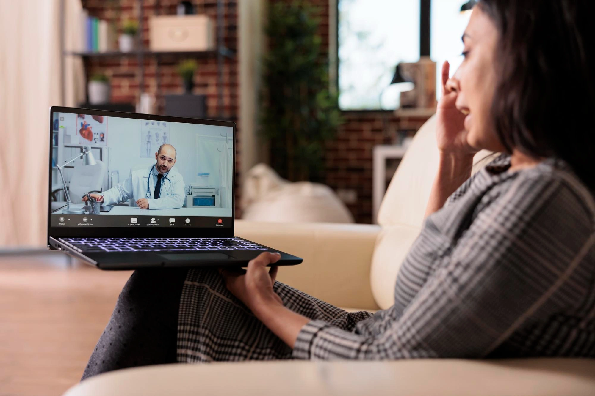 Woman on a sofa with a laptop on her lap during a video call with a doctor
